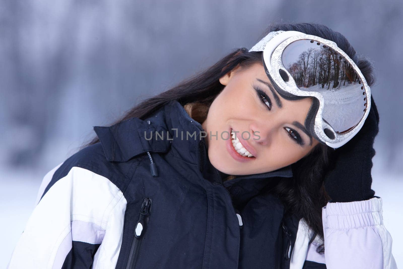 Beautiful woman wearing goggles in snowy winter outdoors