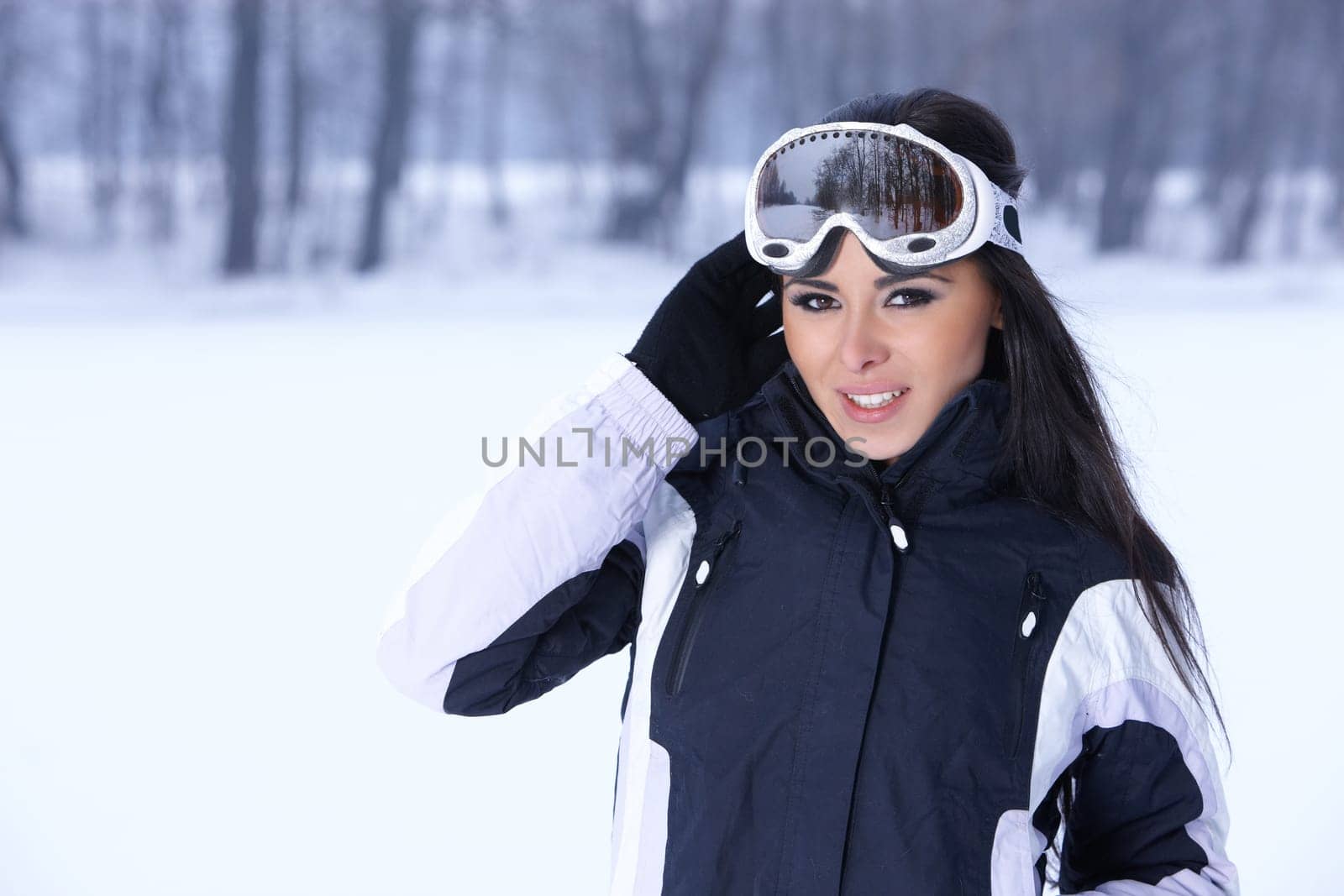 Beautiful woman wearing goggles in snowy winter outdoors