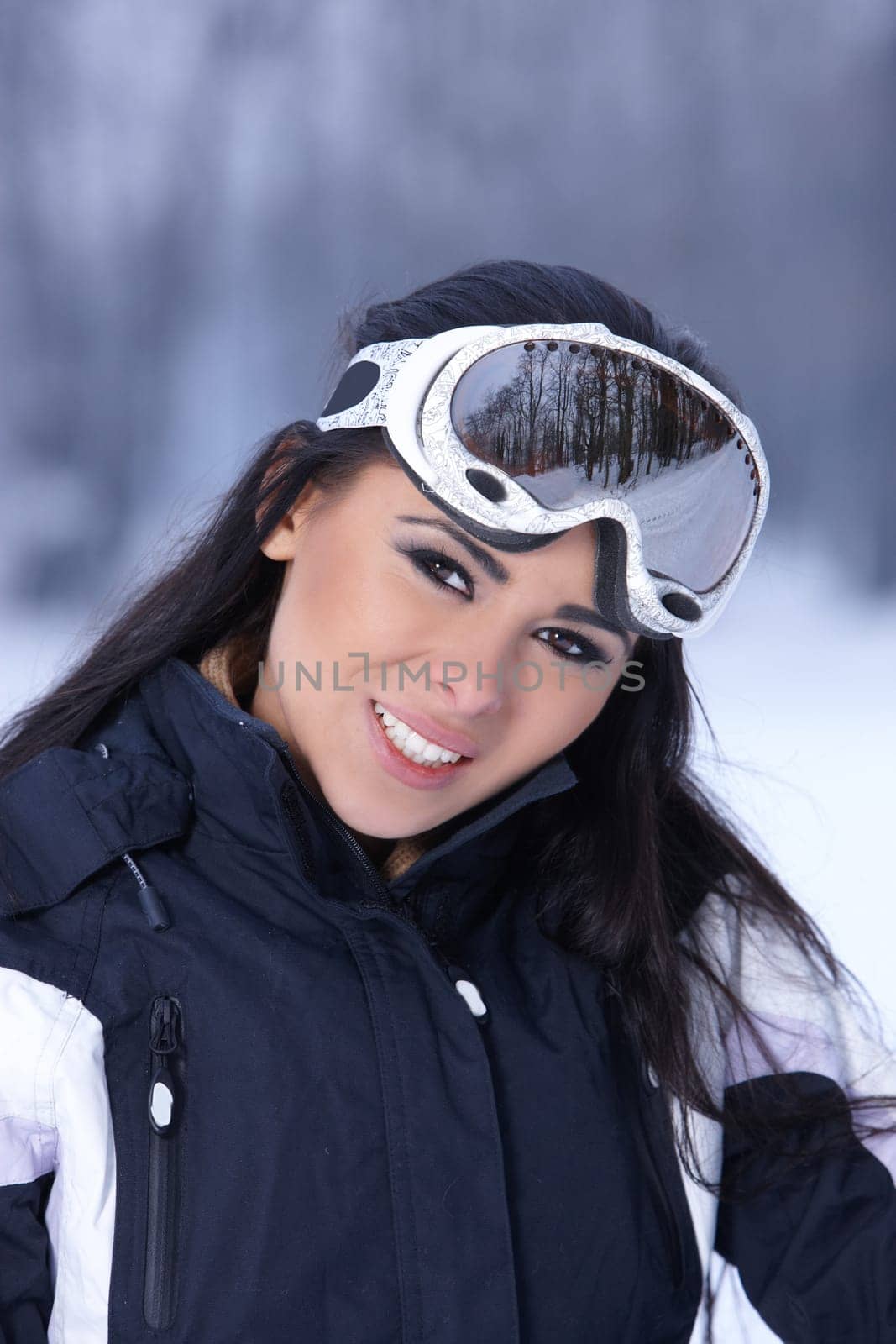 Beautiful woman wearing goggles in snowy winter outdoors