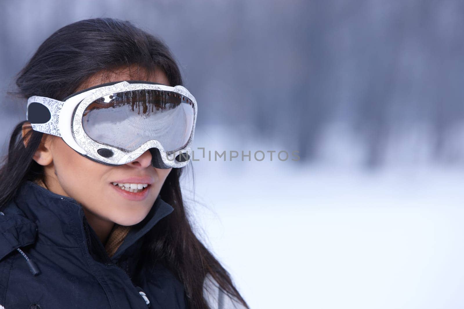 Beautiful woman wearing goggles in snowy winter outdoors