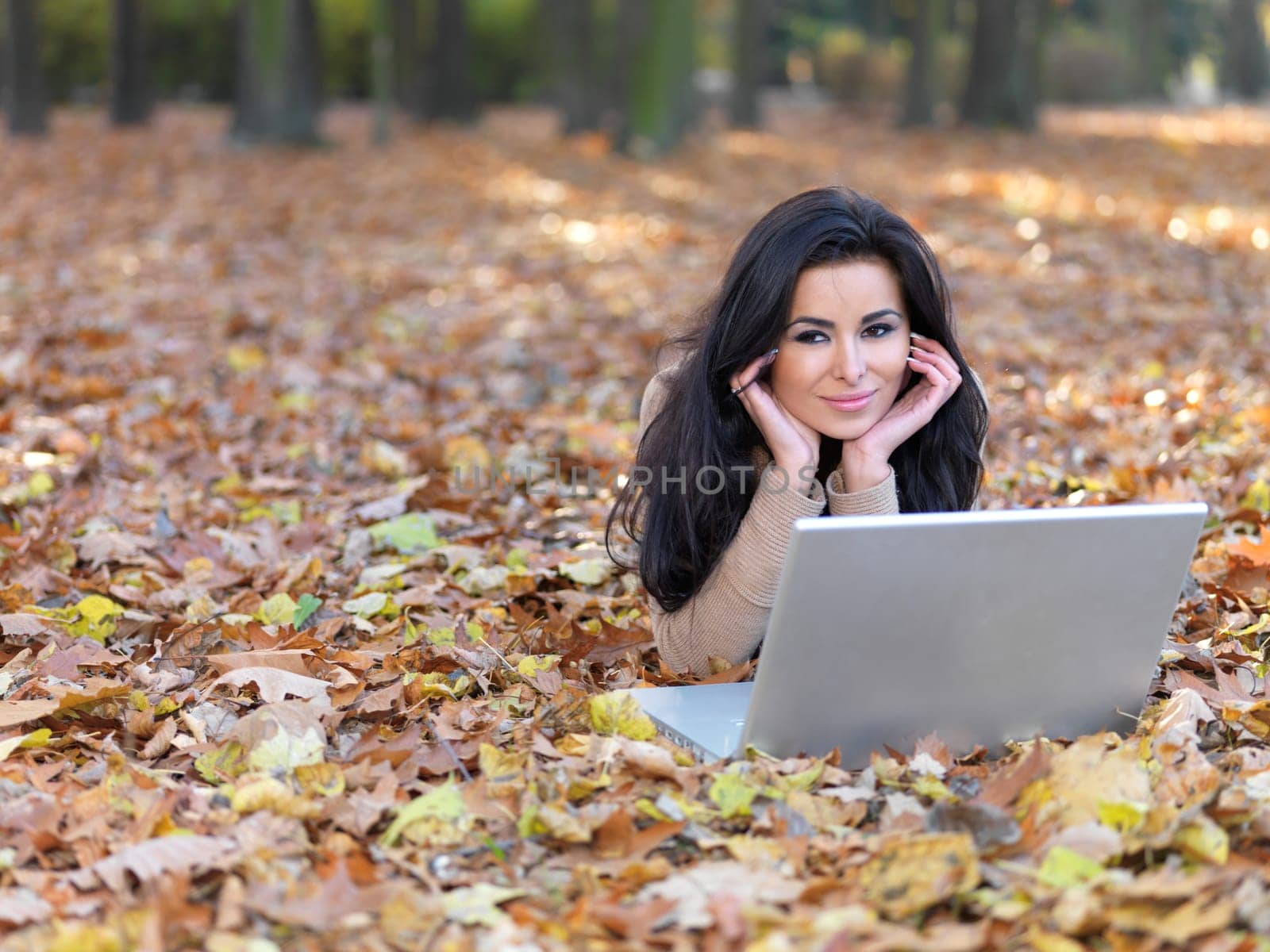 Beautiful woman working on laptop in park during autumn season