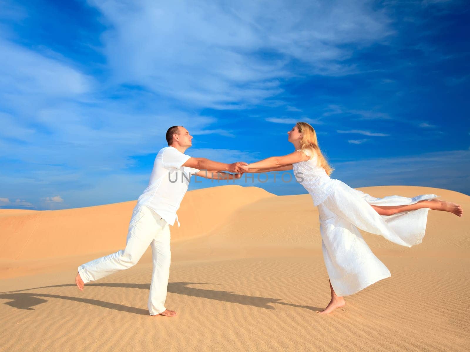 Young couple dancing on desert dune in white clothes