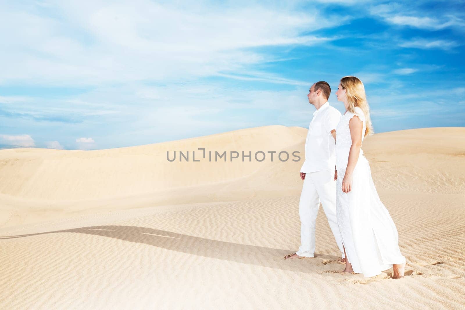 Young couple walking on desert dune in white clothes