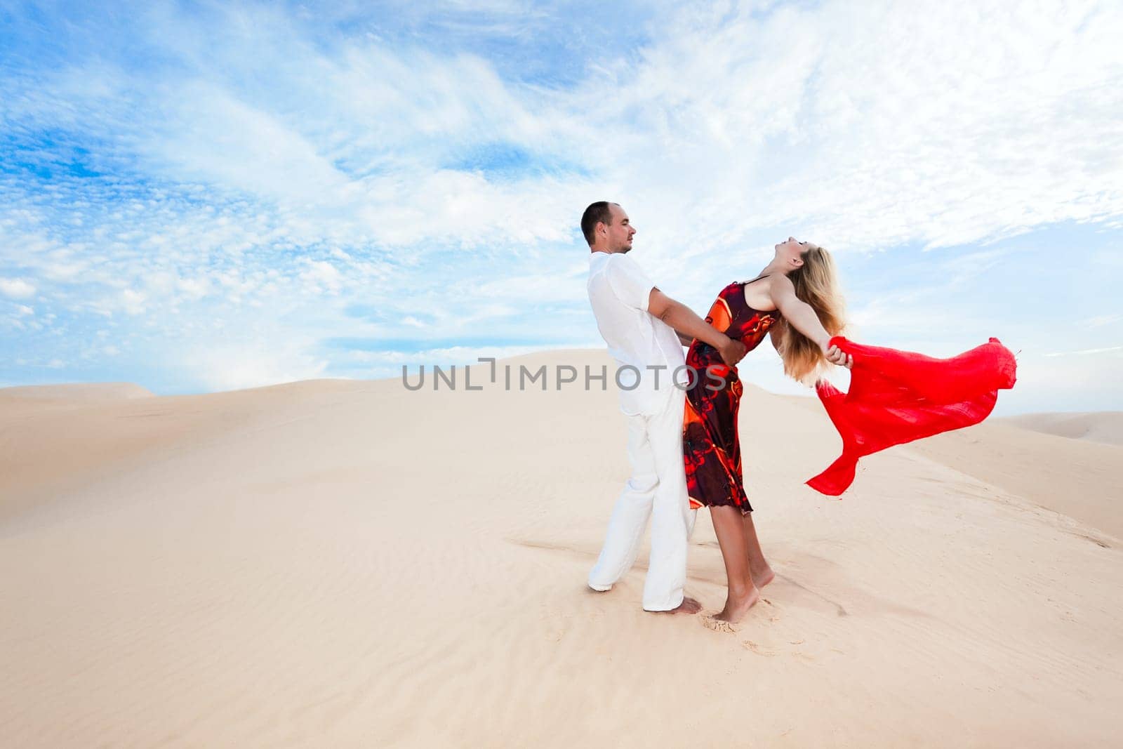 Young couple dancing on desert dune with red scarf