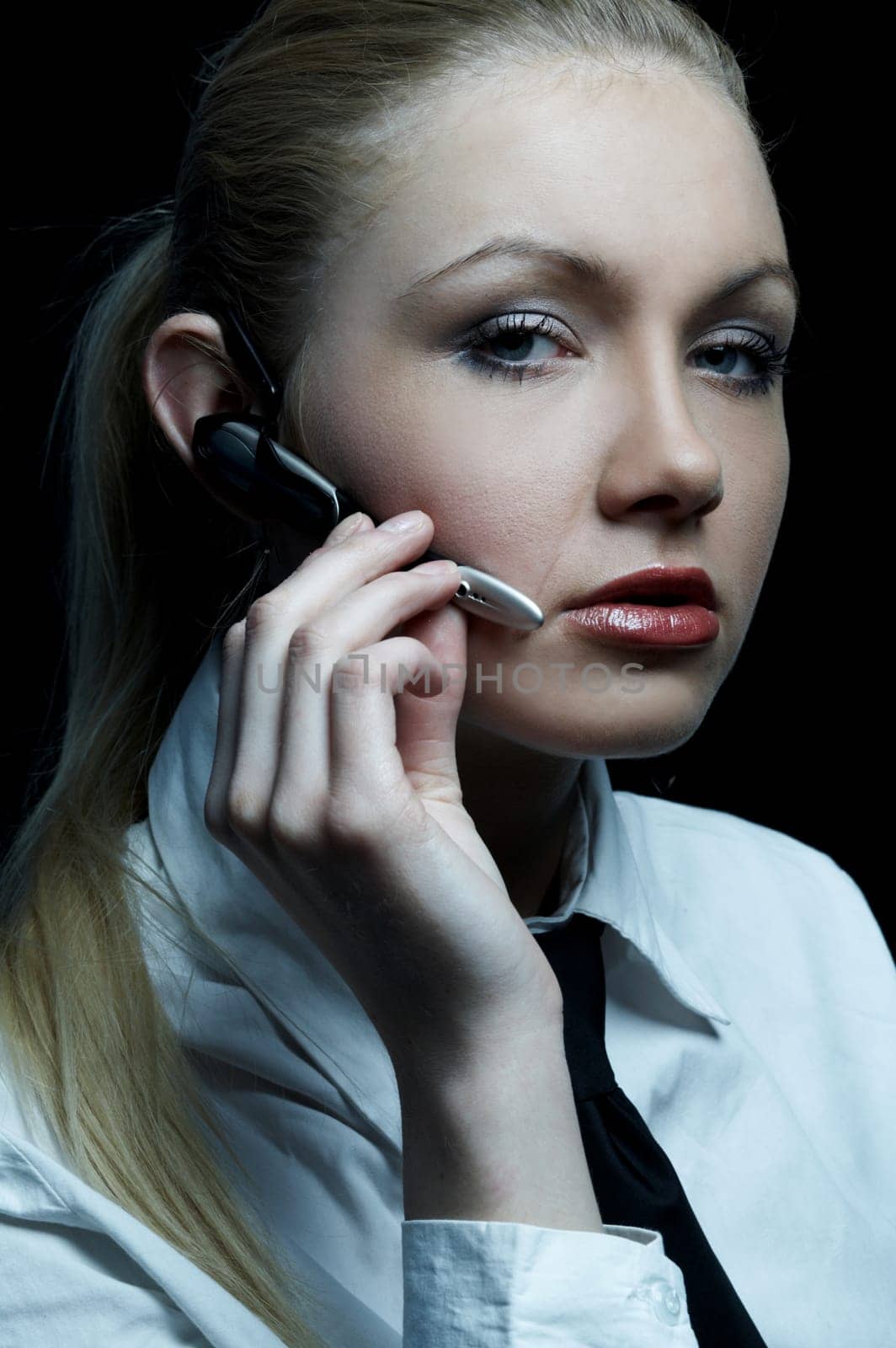 Beautiful business woman wearing black tie and white shirt isolated on black background talking via wireless headset