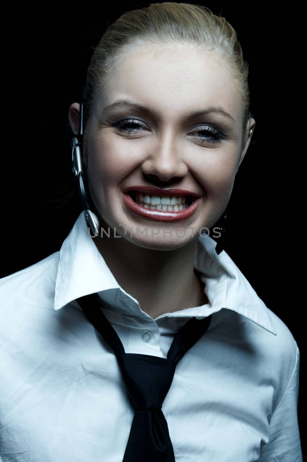 Beautiful business woman wearing black tie and white shirt isolated on black background talking via wireless headset
