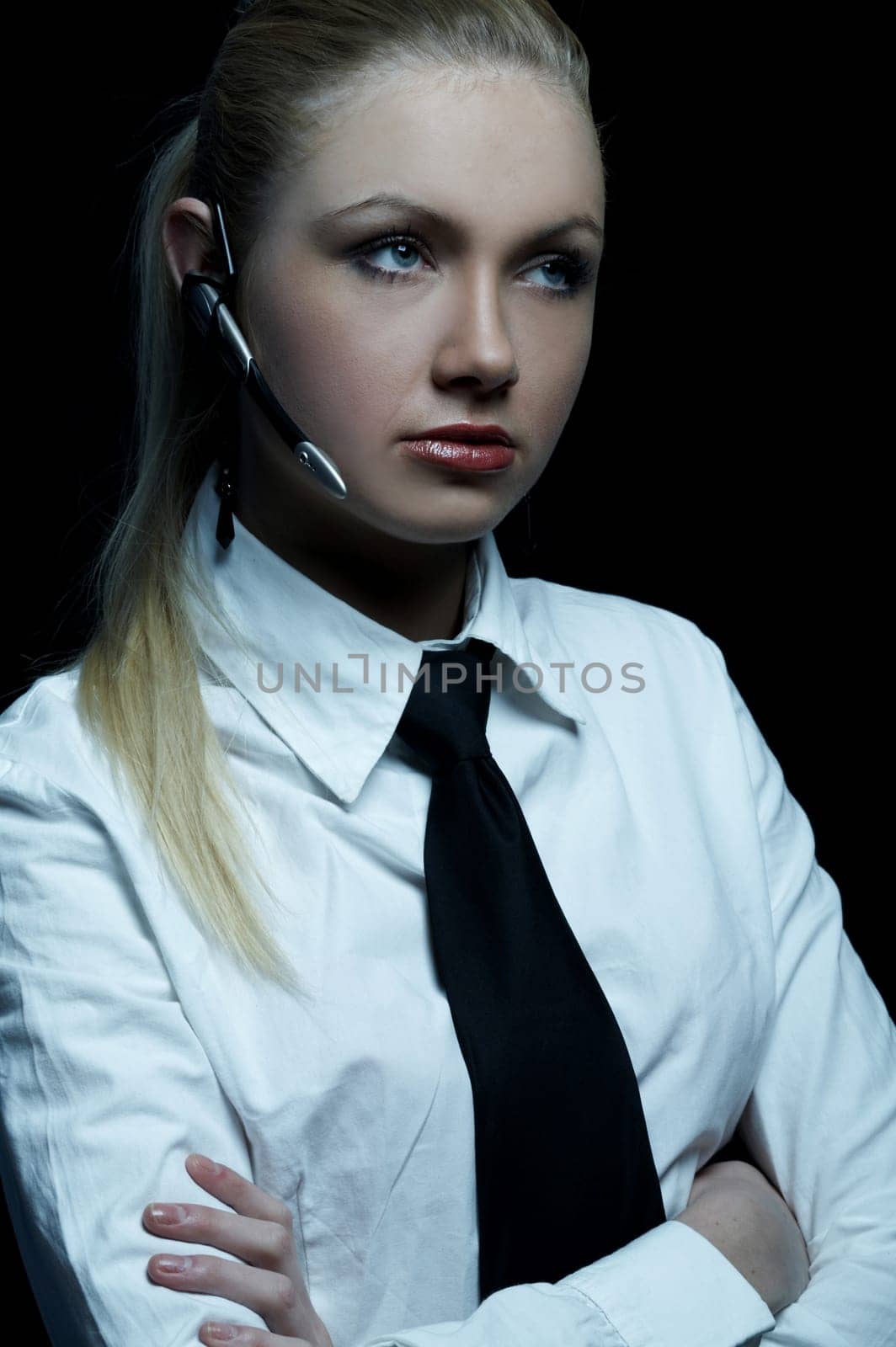 Beautiful business woman wearing black tie and white shirt isolated on black background talking via wireless headset