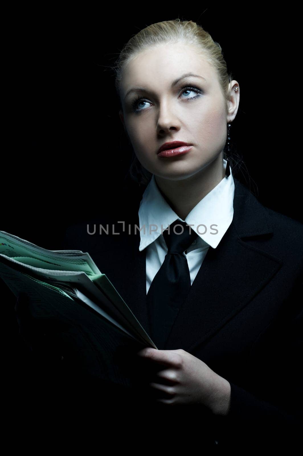 Beautiful business woman wearing black tie and jacket isolated on black background holding newspaper
