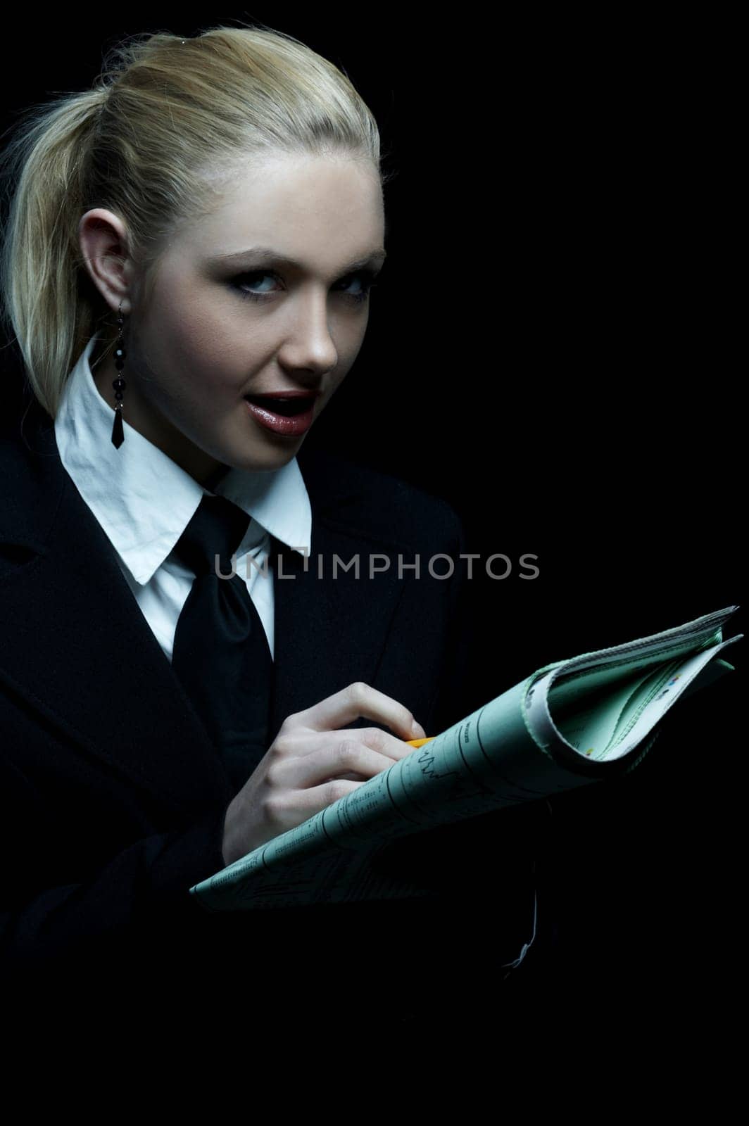 Beautiful business woman wearing black tie and jacket isolated on black background holding newspaper