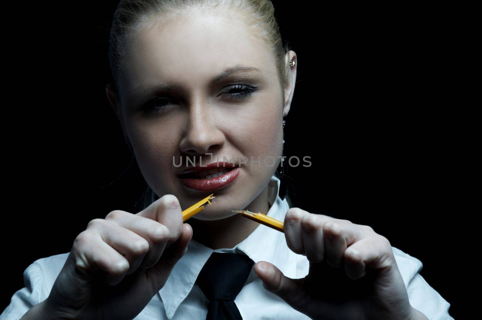 Beautiful business woman wearing black tie and white shirt isolated on black background holding broken pencil