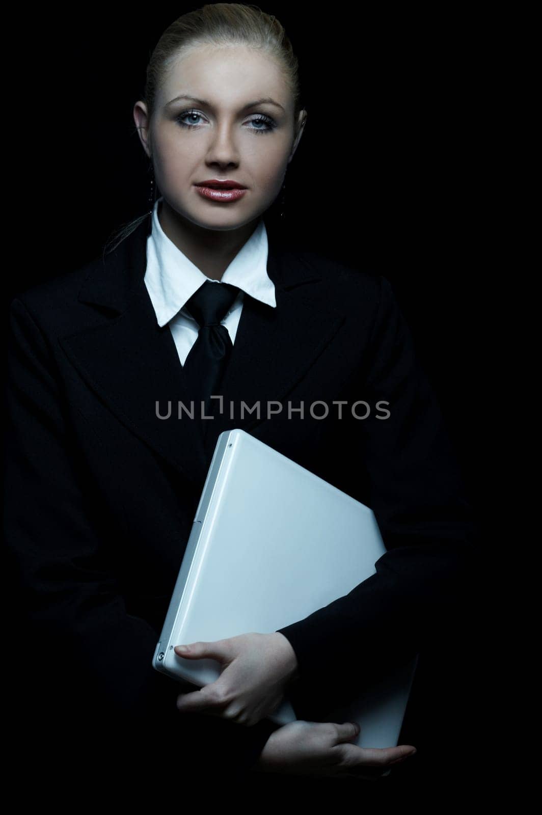 Beautiful business woman wearing black tie and jacket isolated on black background with laptop computer