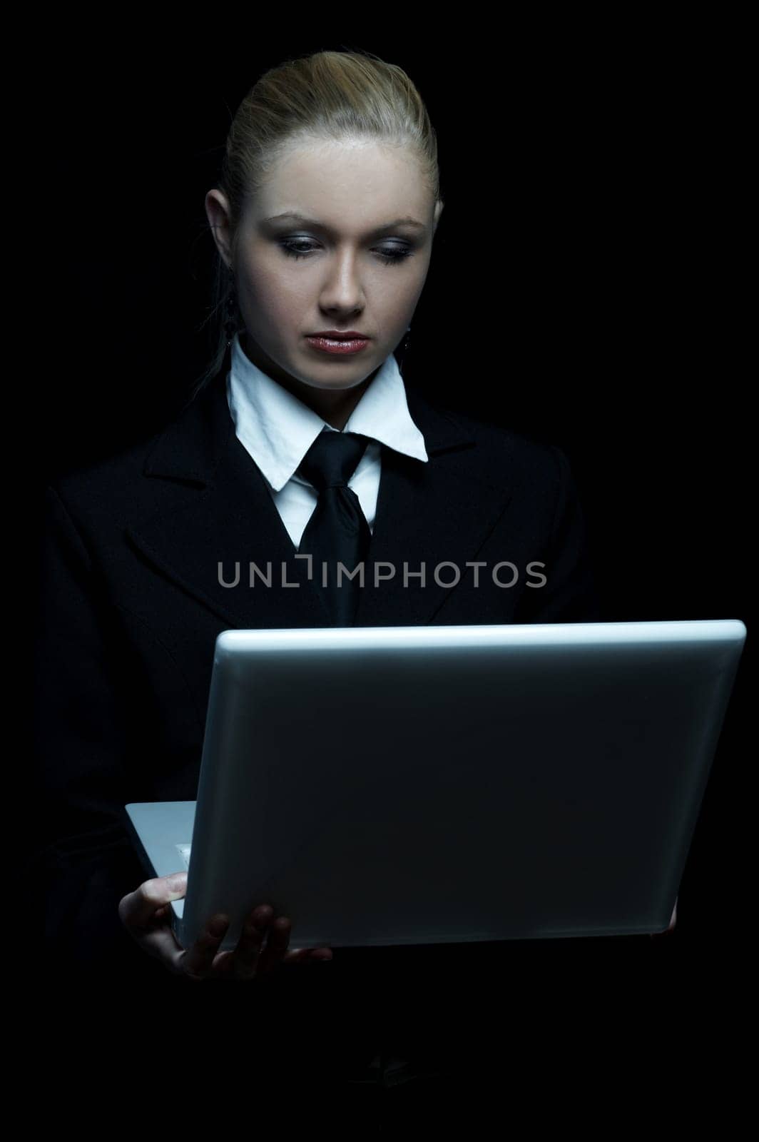 Beautiful business woman wearing black tie and jacket isolated on black background with laptop computer