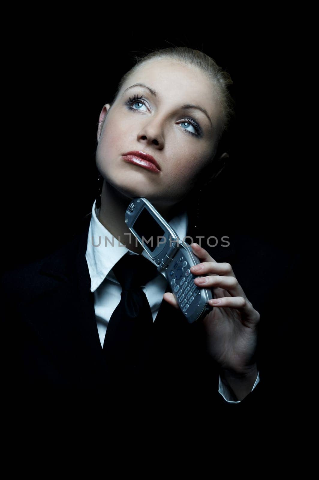 Beautiful business woman wearing black tie and jacket isolated on black background with cell phone