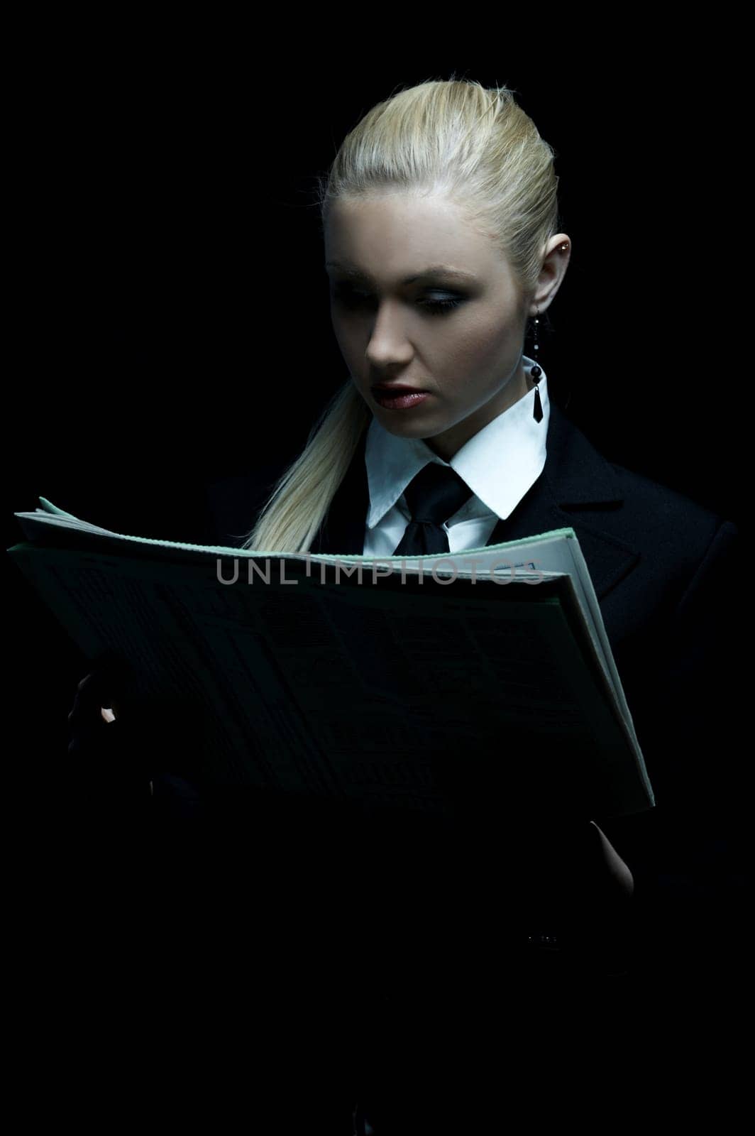 Beautiful business woman wearing black tie and jacket isolated on black background holding newspaper
