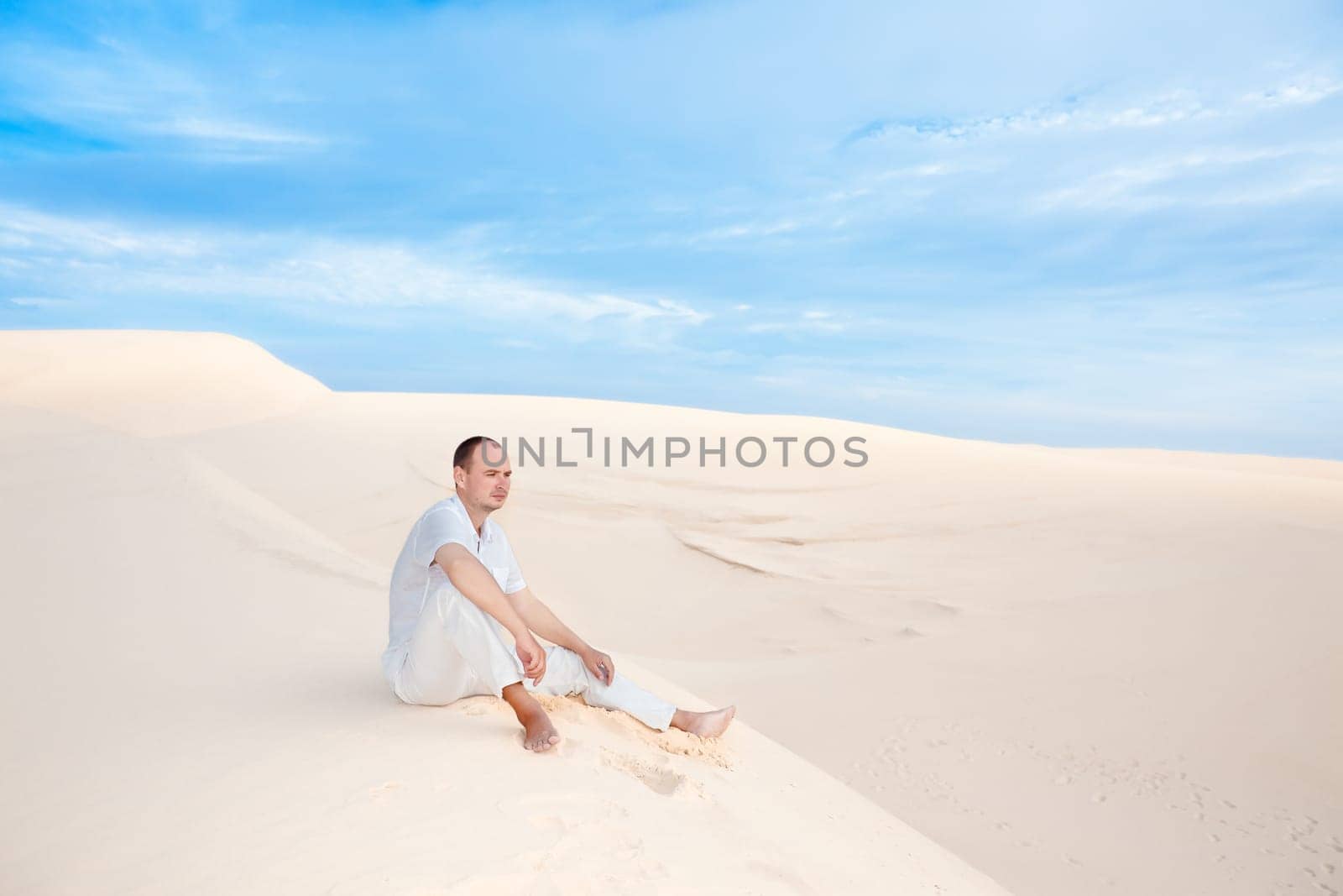 Young lonely man sitting in the middle of desert