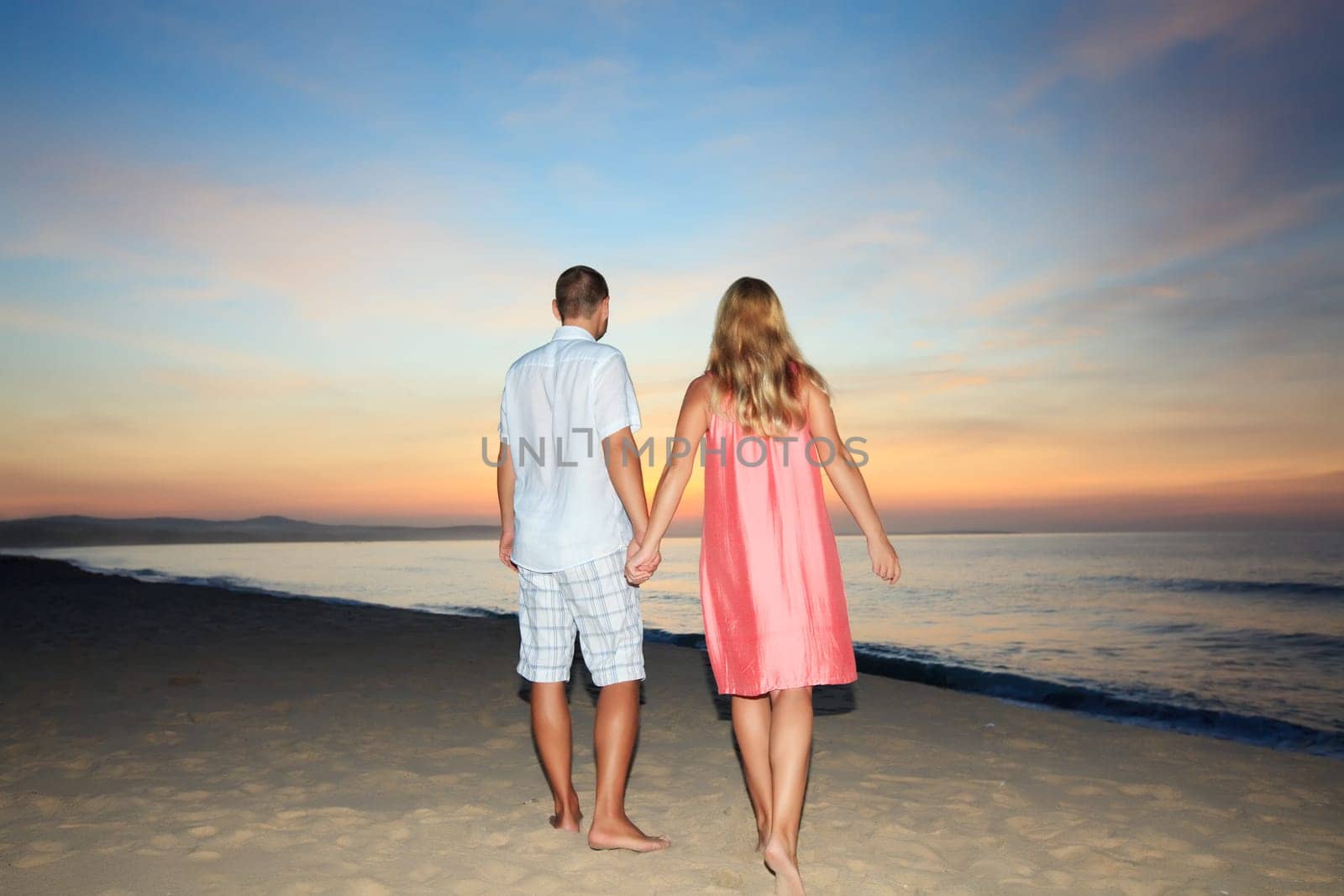 Couple walking on the beach at sunrise time.