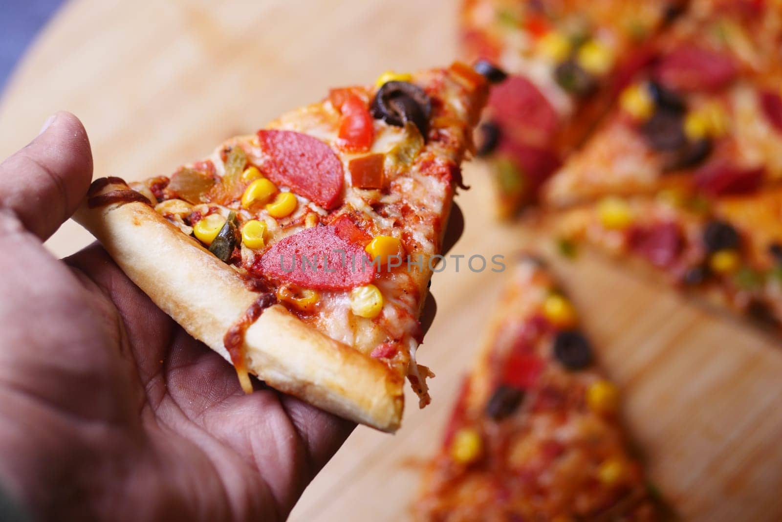 A hand holds a slice of pizza topped with vegetables and pepperoni.