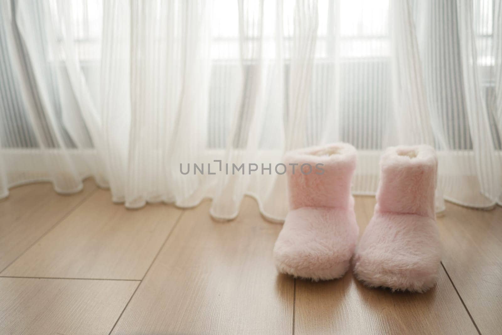 Soft pink slippers rest on the warm wooden floor by the curtain-draped window.