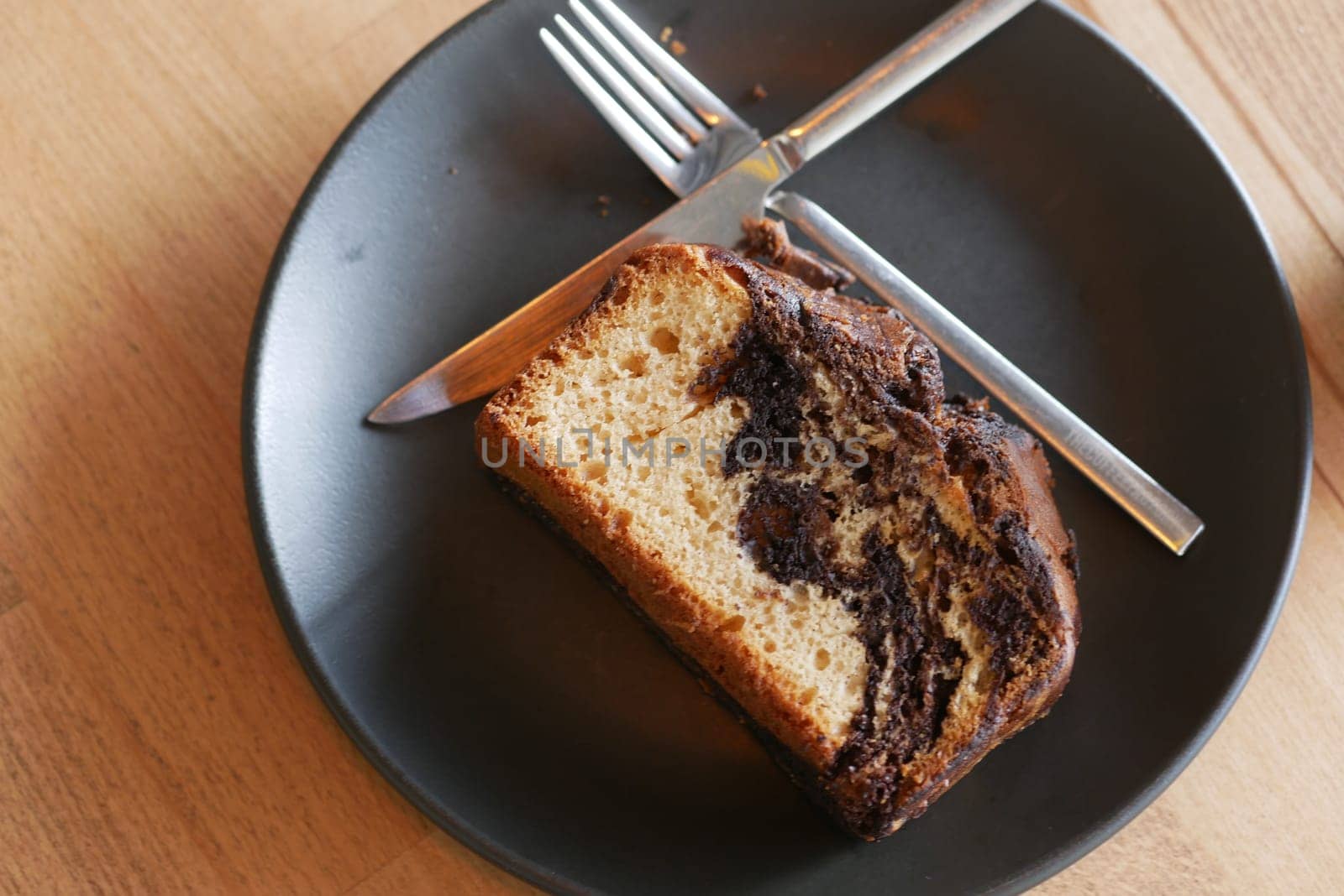 A slice of chocolate marble cake rests on a black plate with cutlery.