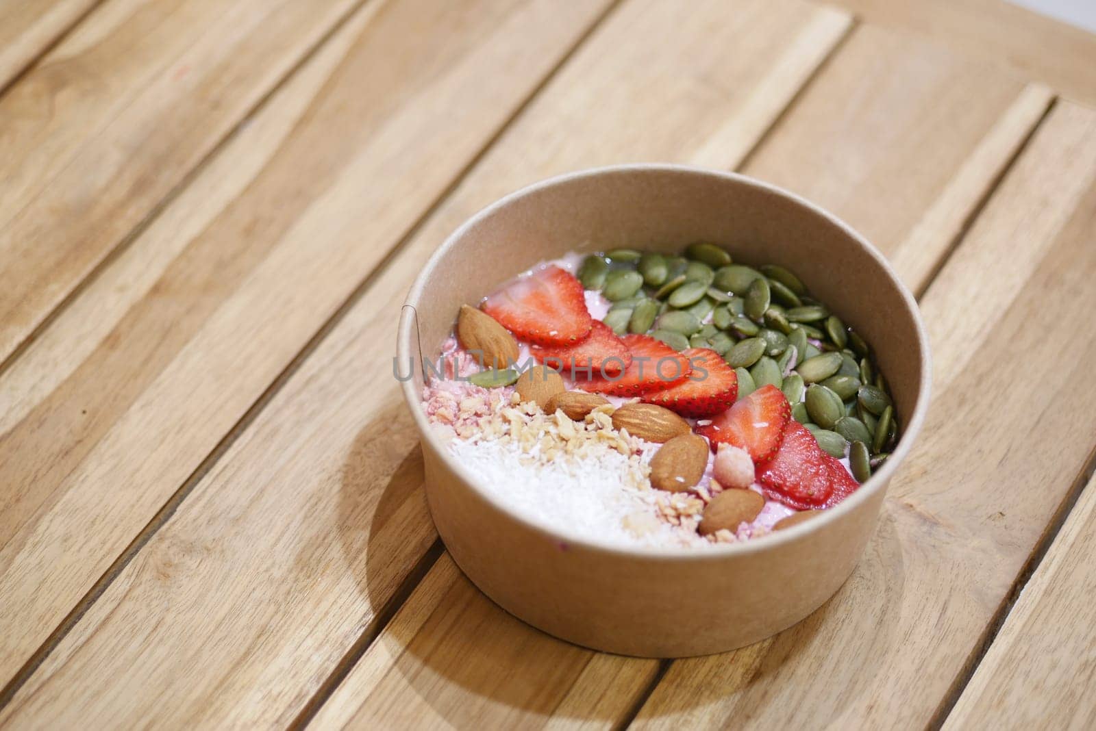 Colorful smoothie bowl topped with fruits and nuts on a wooden surface.
