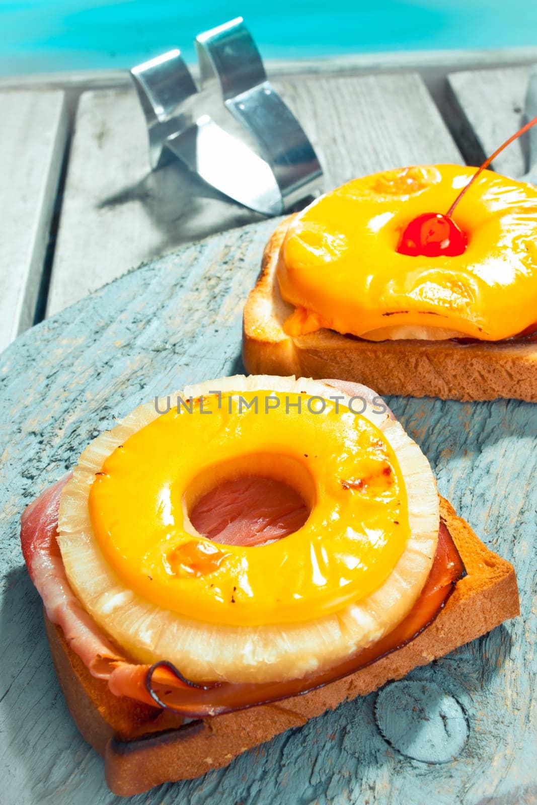 Exotic open ham and pineapple sandwich topped with a ring of golden melted cheese sreved on a deck alongside a pool