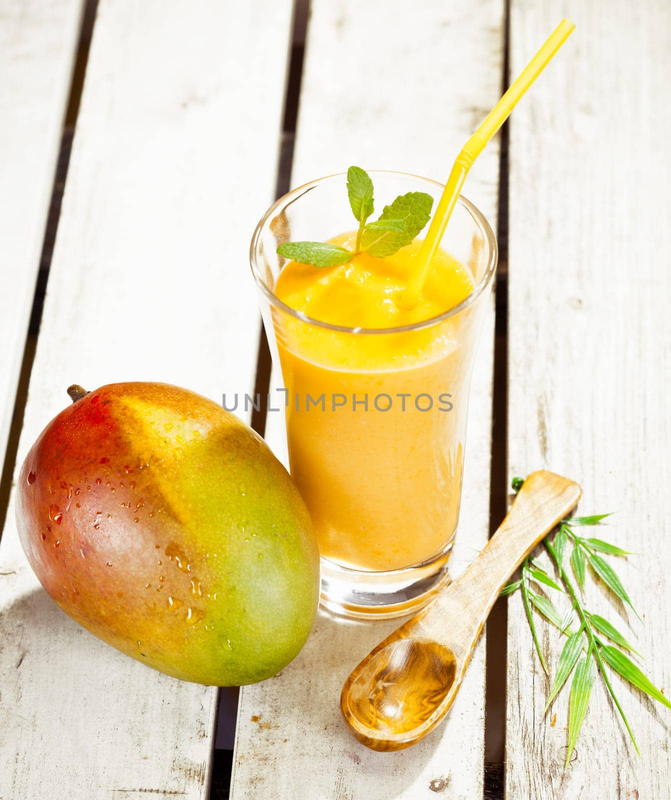 High angle view of a glass of healthy fresh mango smoothie with a delicious ripe whole fruit alongside on wooden decking