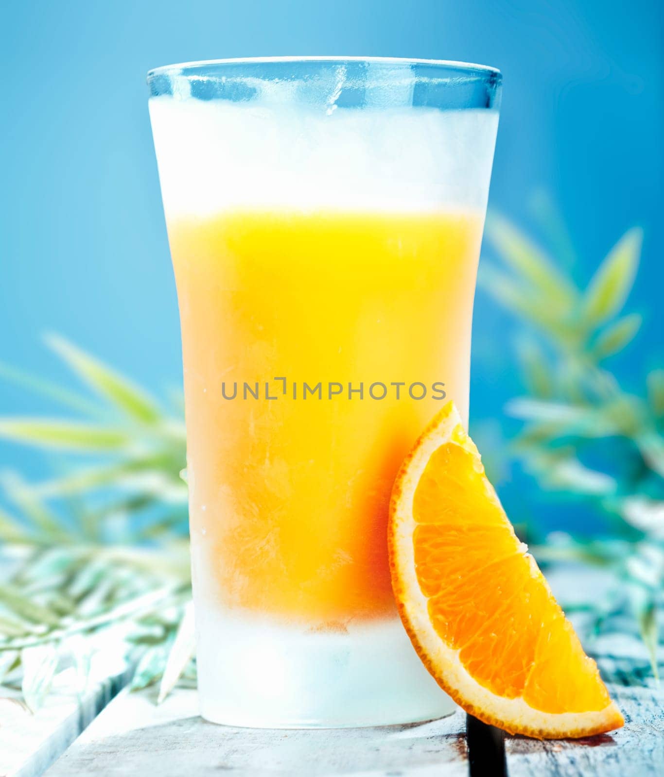 Tall glass of chilled orange cocktail with freshly squeezed juice against a blue summer sky