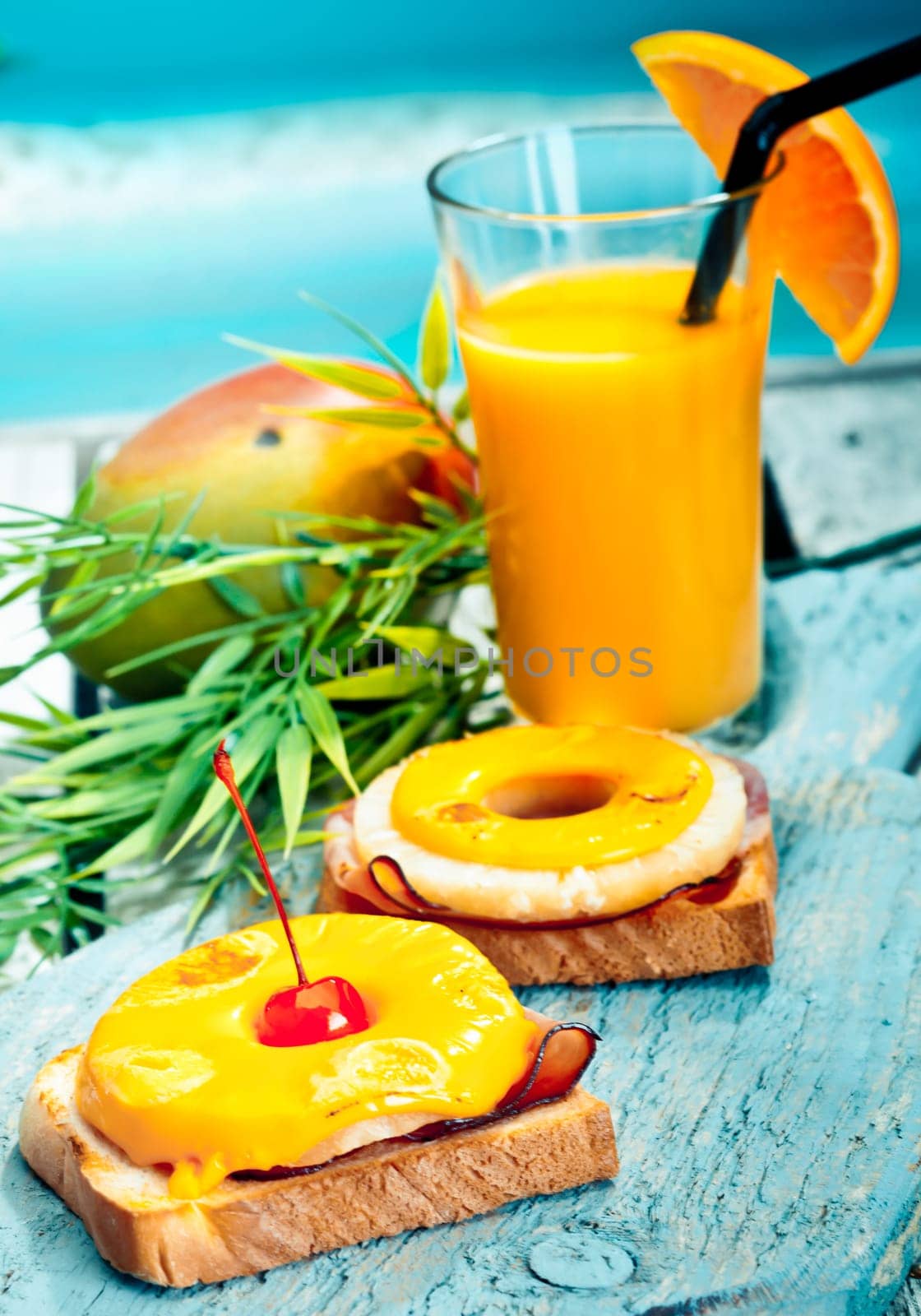 Colourful healthy tropical lunch of open ham and pineapple sandwiches topped with melted cheese accompanied by fresh mango juice