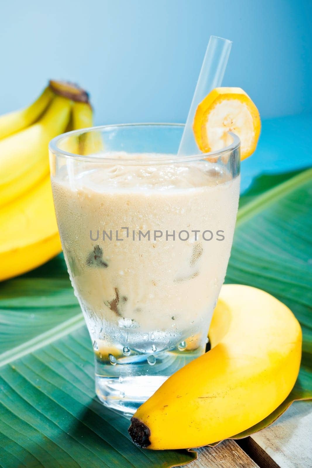 Creamy banana smoothie blended with fresh yoghurt in a glass with ripe bananas and a banana leaf