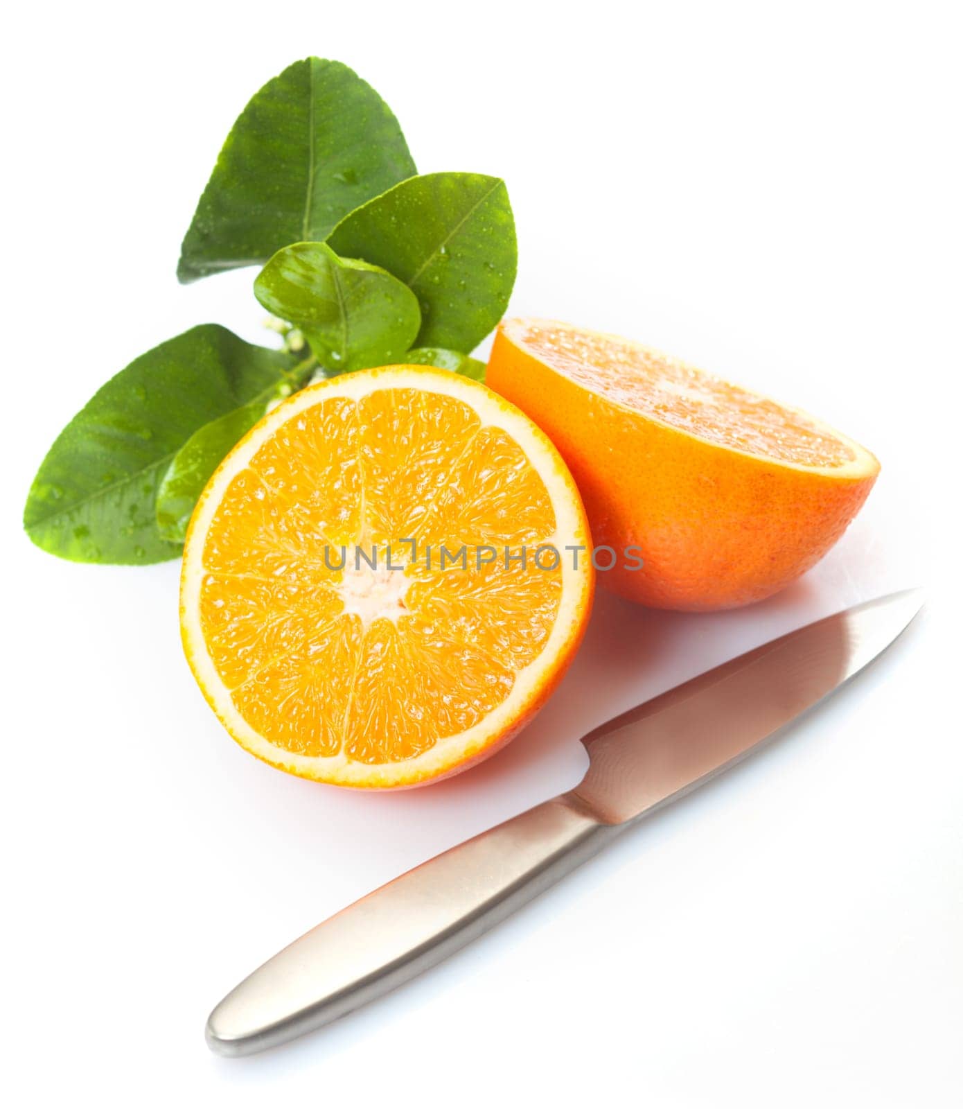 Fresh halved orange with citrus leaves and a knife on a white studio background
