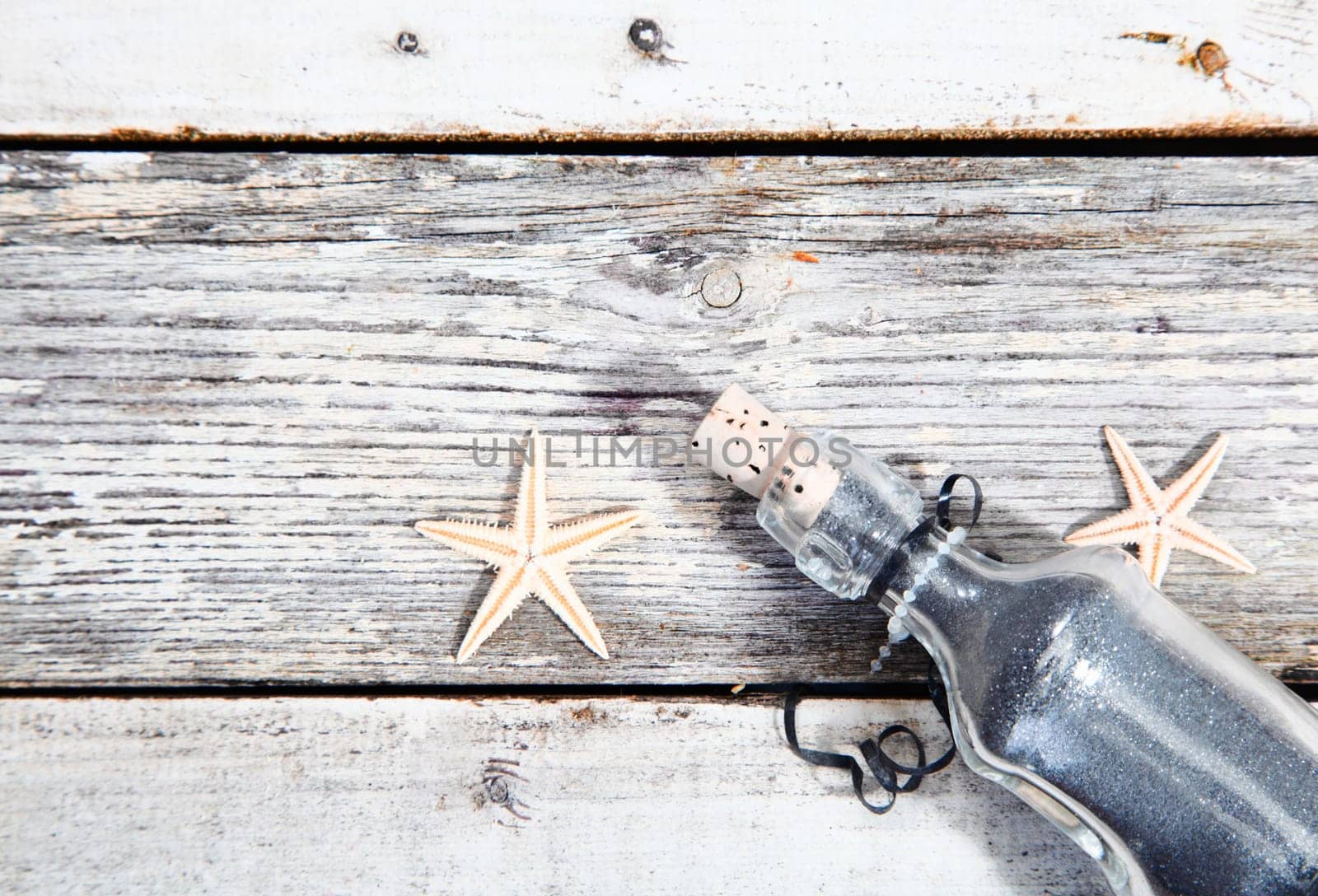 Nautical background with starfish and a clear glass corked bottle on weathered timber planks with woodgrain