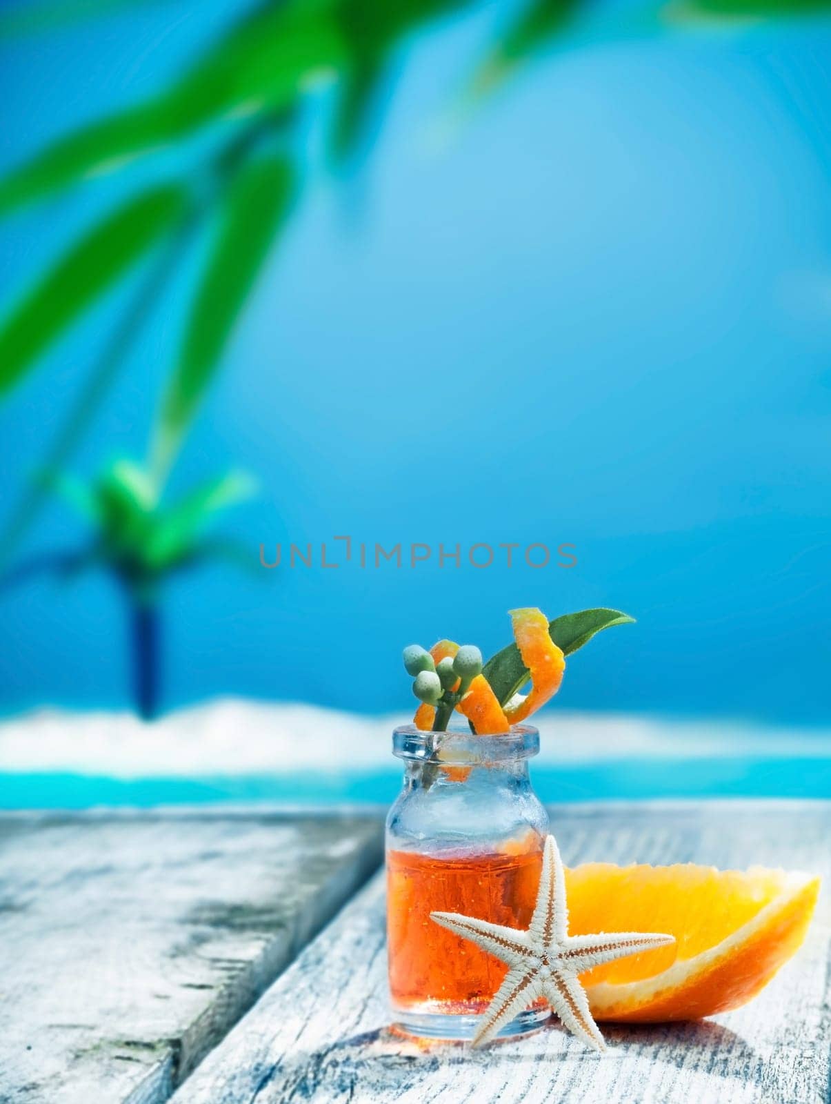 A small glass bottle of orange essential oil plant extract standing on a wooden seaside deck ready for a tropical spa treatment