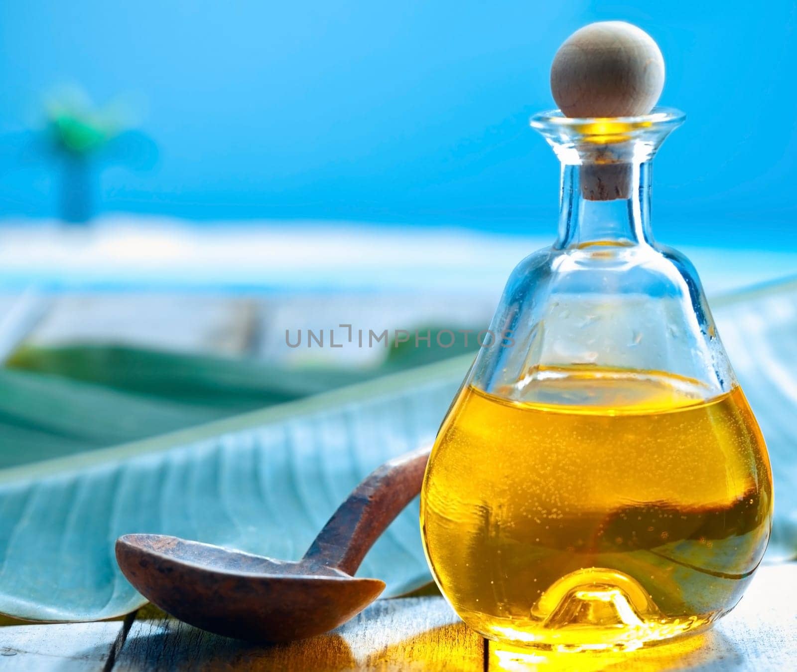 Bottle of glowing golden oil and a ladle on a deck near the sea ready for a tropical spa treatment