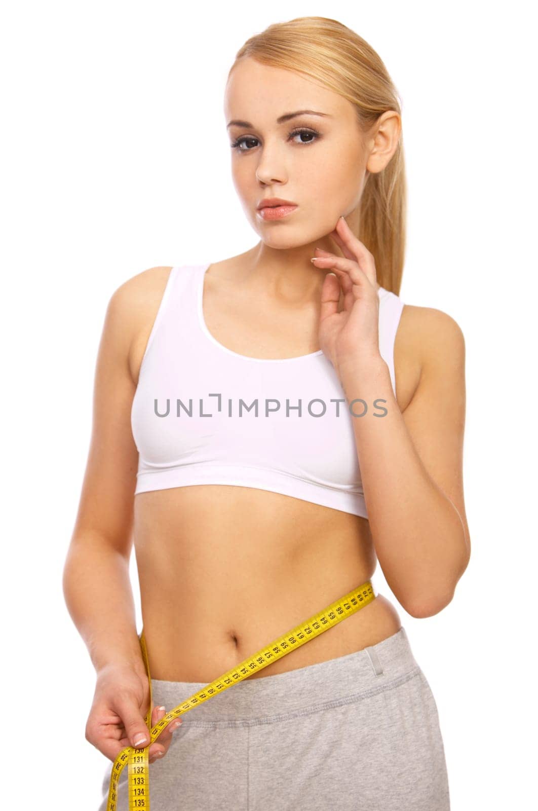 Sporty beautiful girl is measuring her waist on white