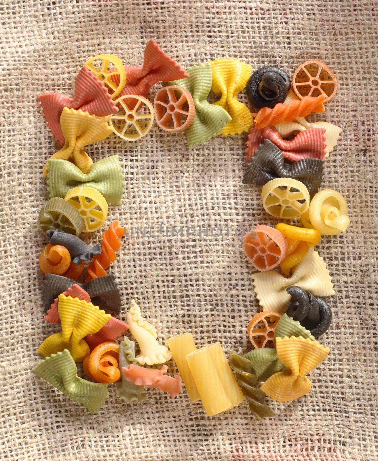 Coulorful frame on hessian material of variously shaped pastas including bowtie, wheels, and spirals.