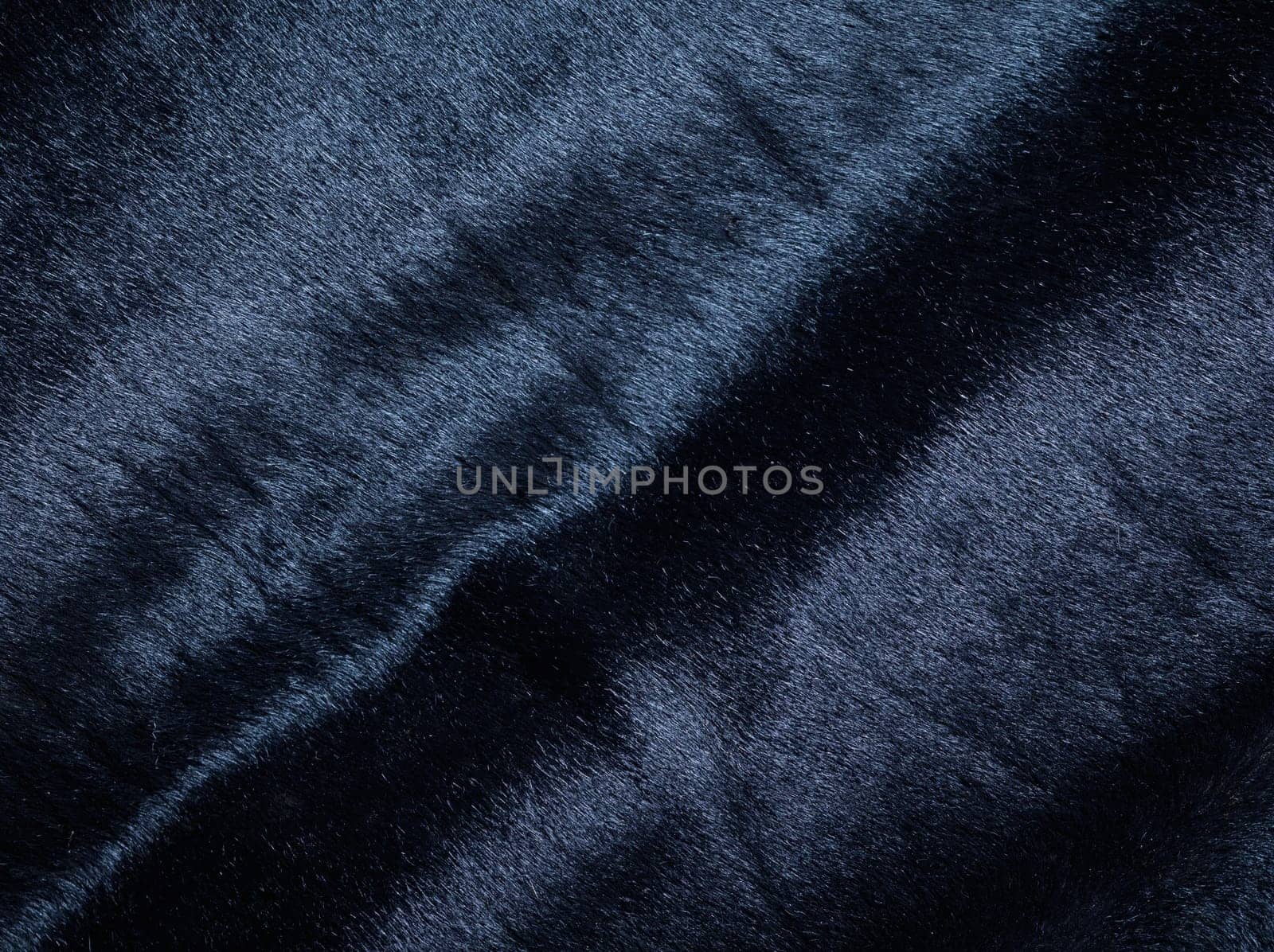 Background of a dark piece of soft supple suede leather with wrinkles
