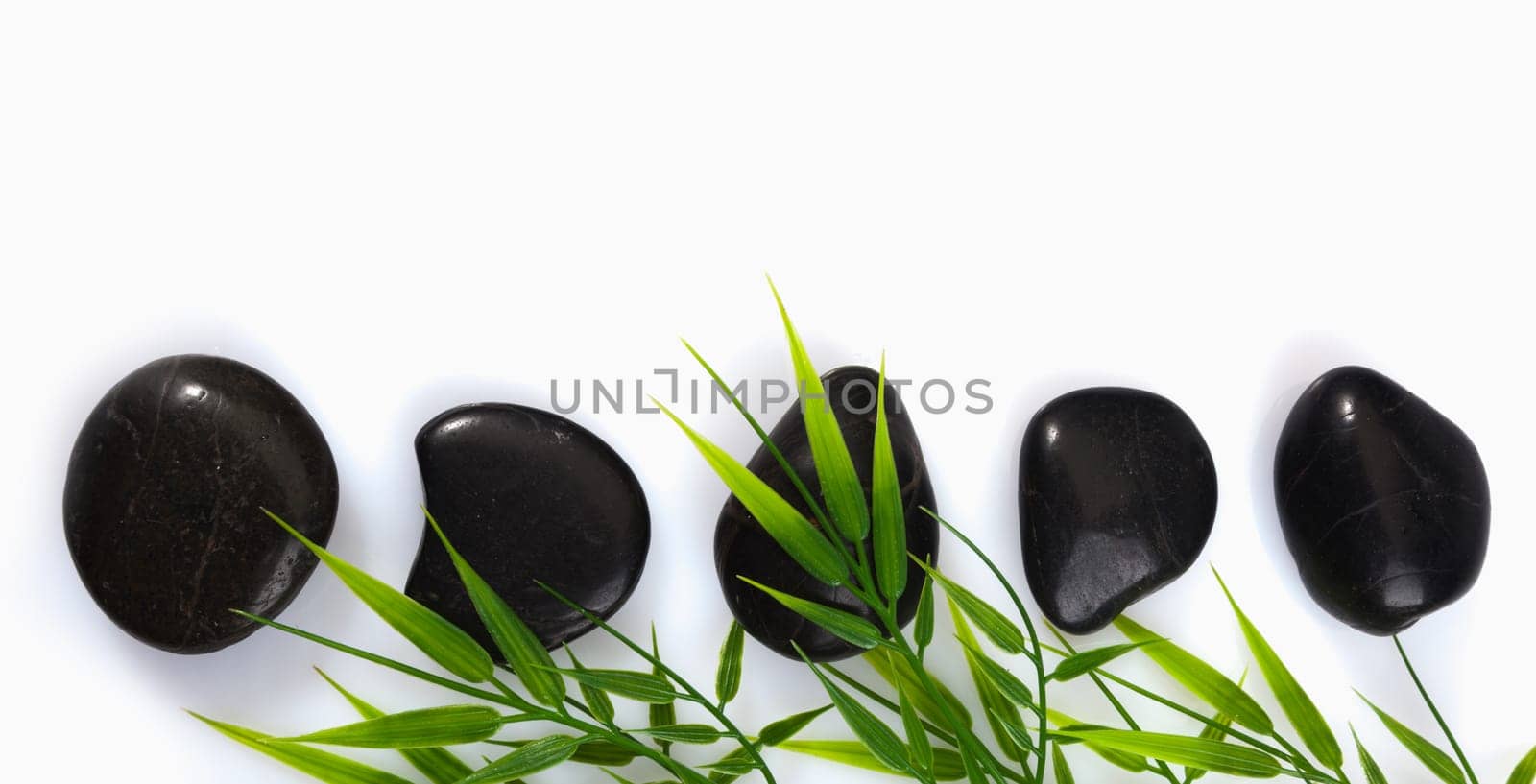 A row of spa massage stones and bamboo leaves on a white background with copyspace