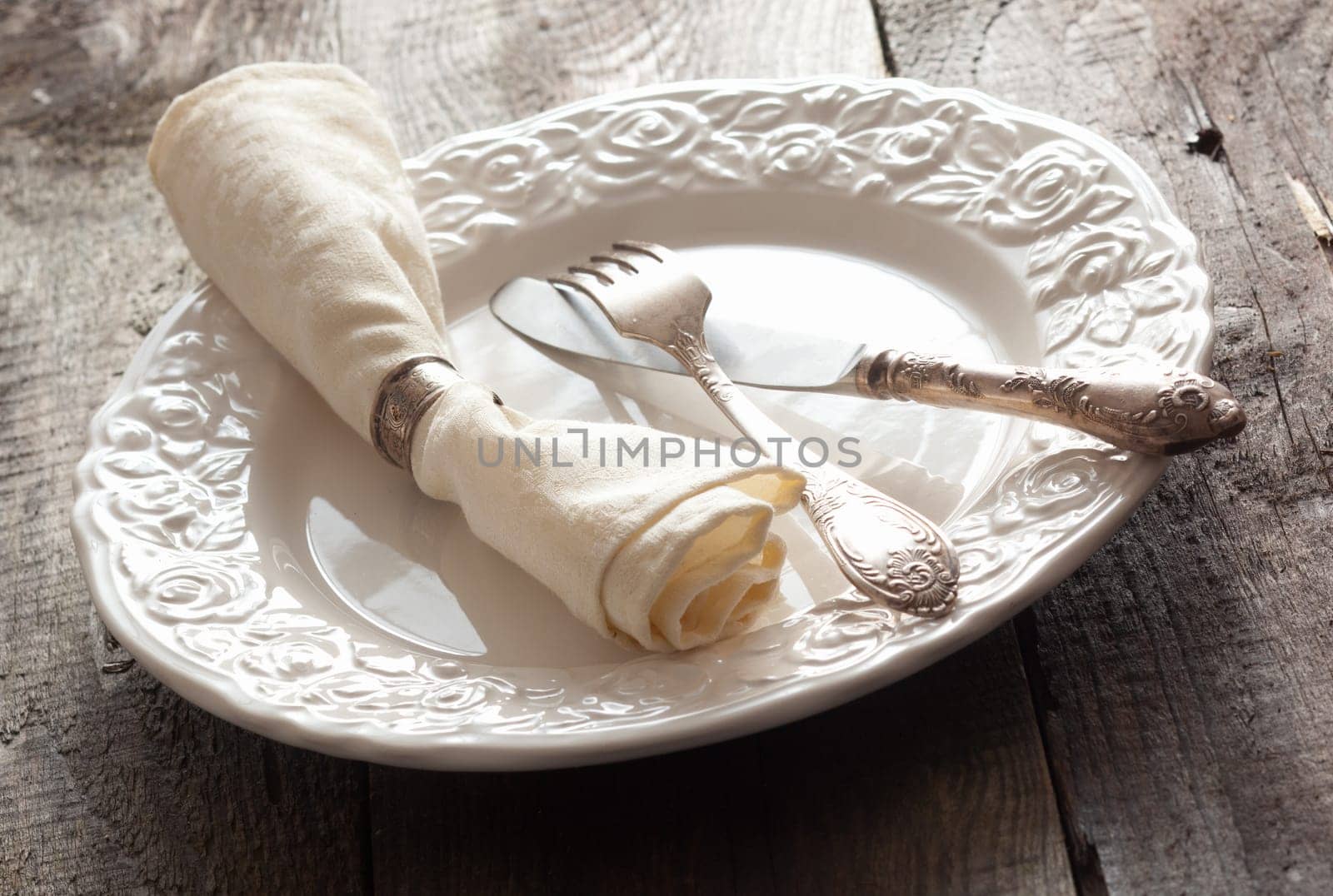 White rose patterned dinner plate with silverware and a napkin in an informal table setting