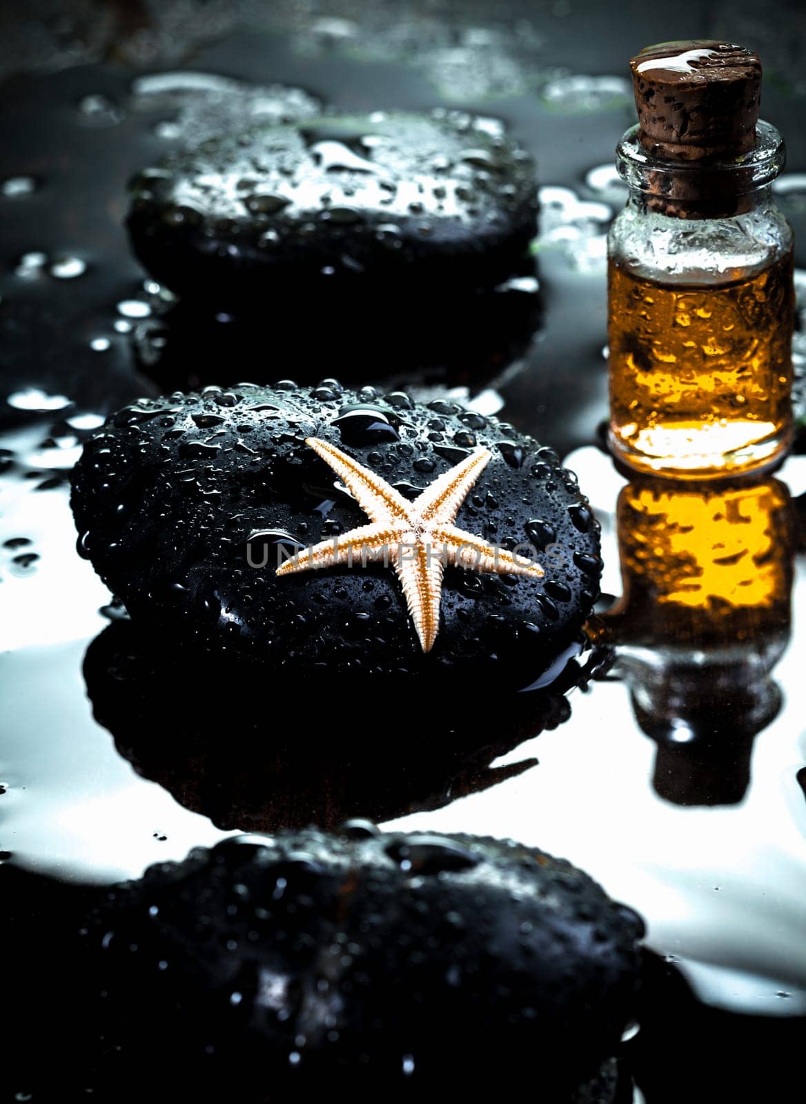 Starfish laying on a basalt stone and massage oils covered with water drops