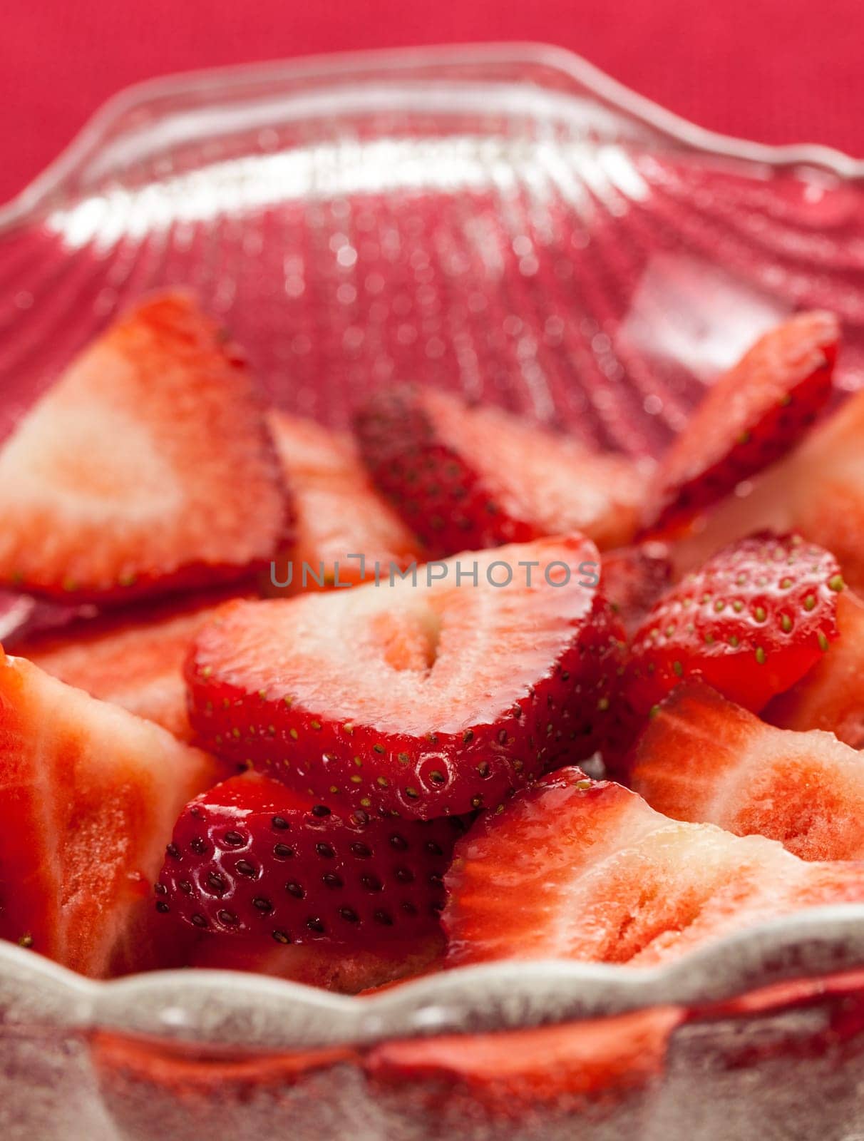 Glass dish with freshly sliced strawberry fruits against a red tablecloth