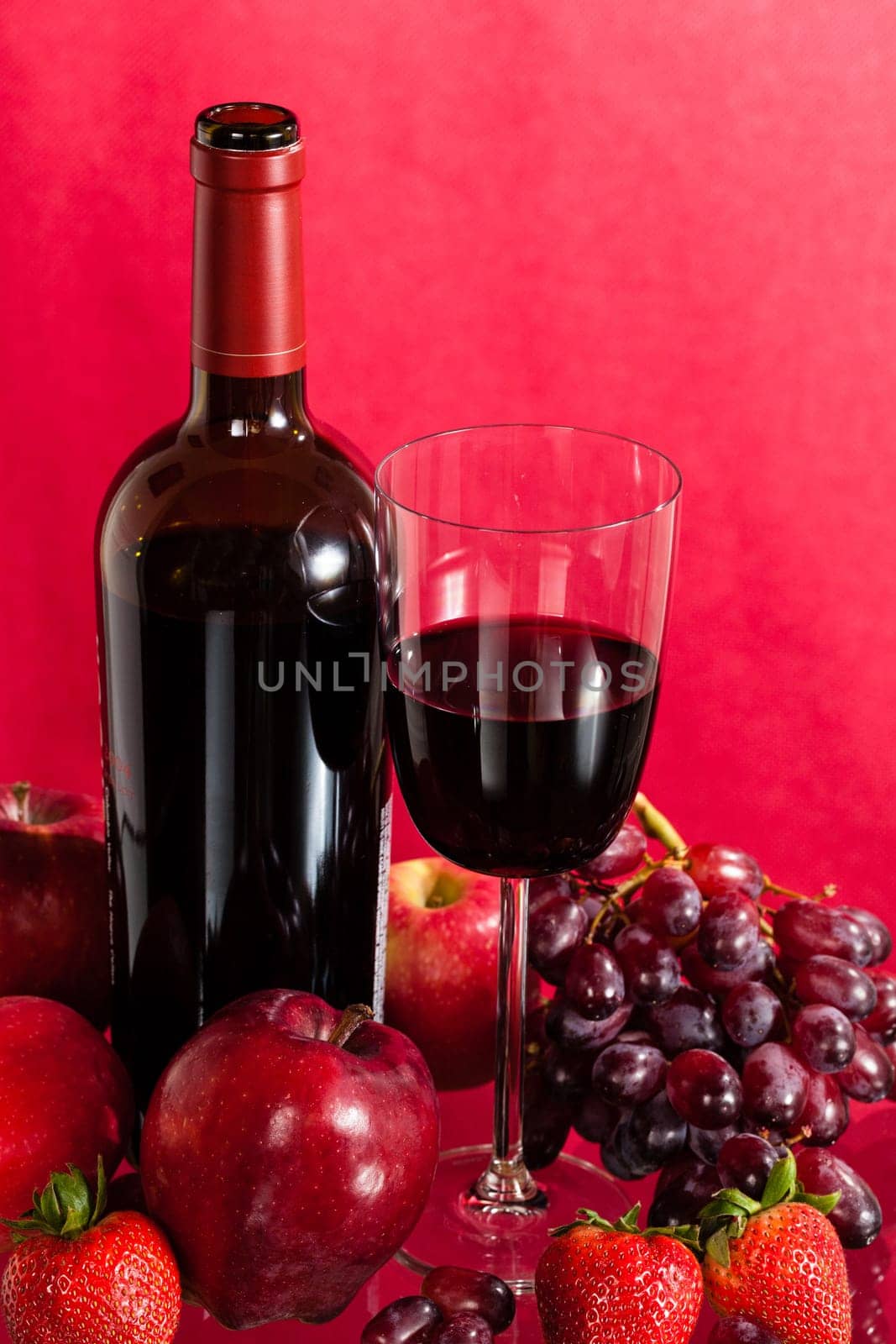 Red wine bottle and red wine in glass with red apples, grapes and strawberries