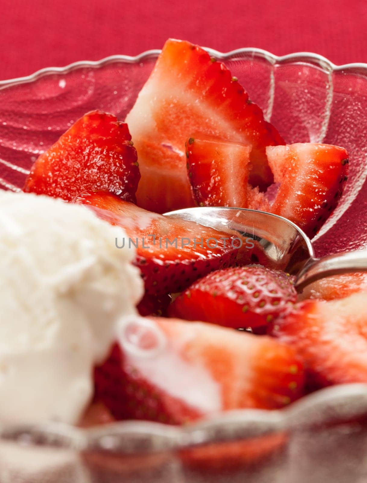 Glass dish with freshly sliced strawberry fruits against a red tablecloth with icecream