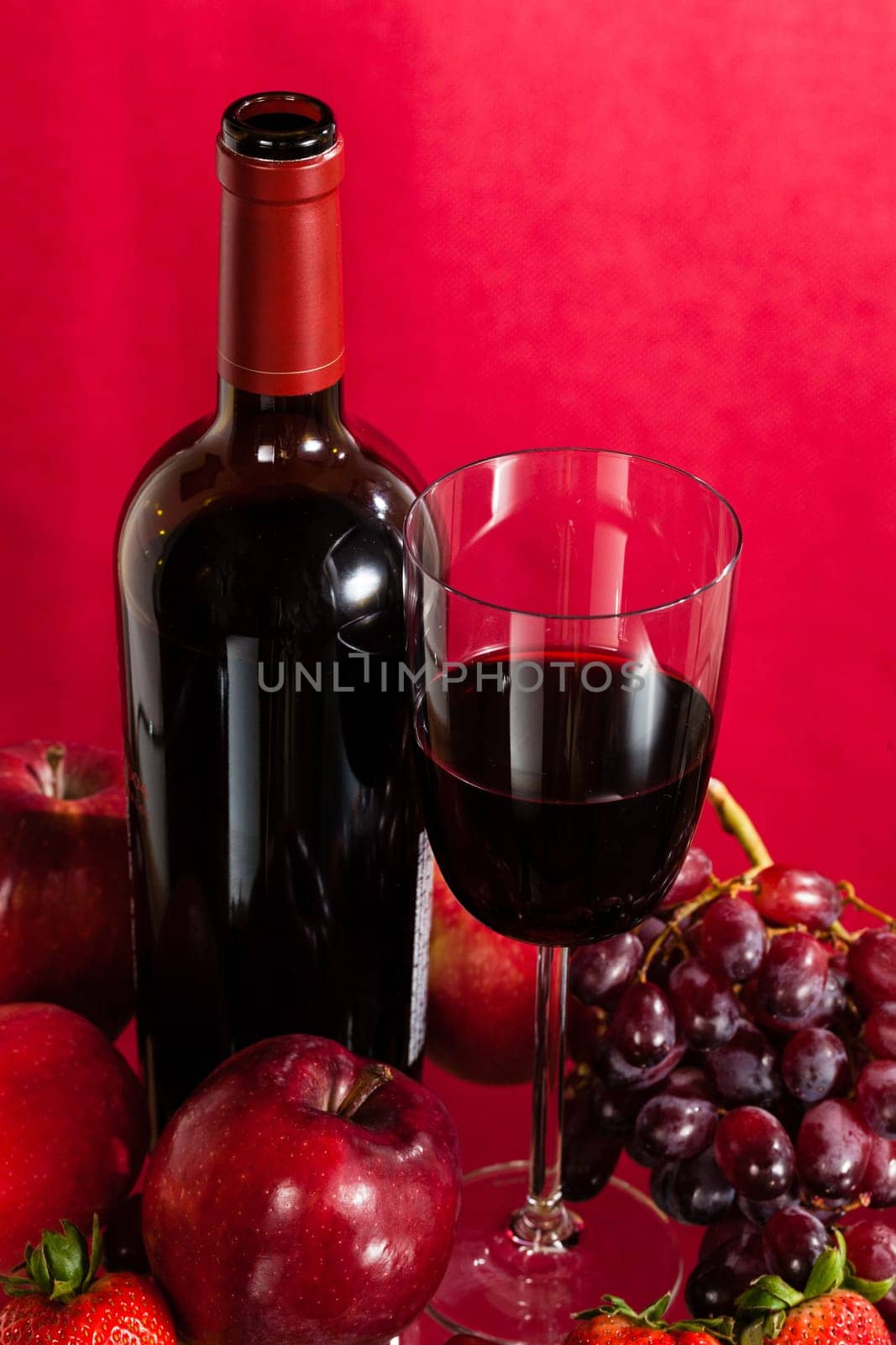 Red wine bottle and red wine in glass with red apples, grapes and strawberries