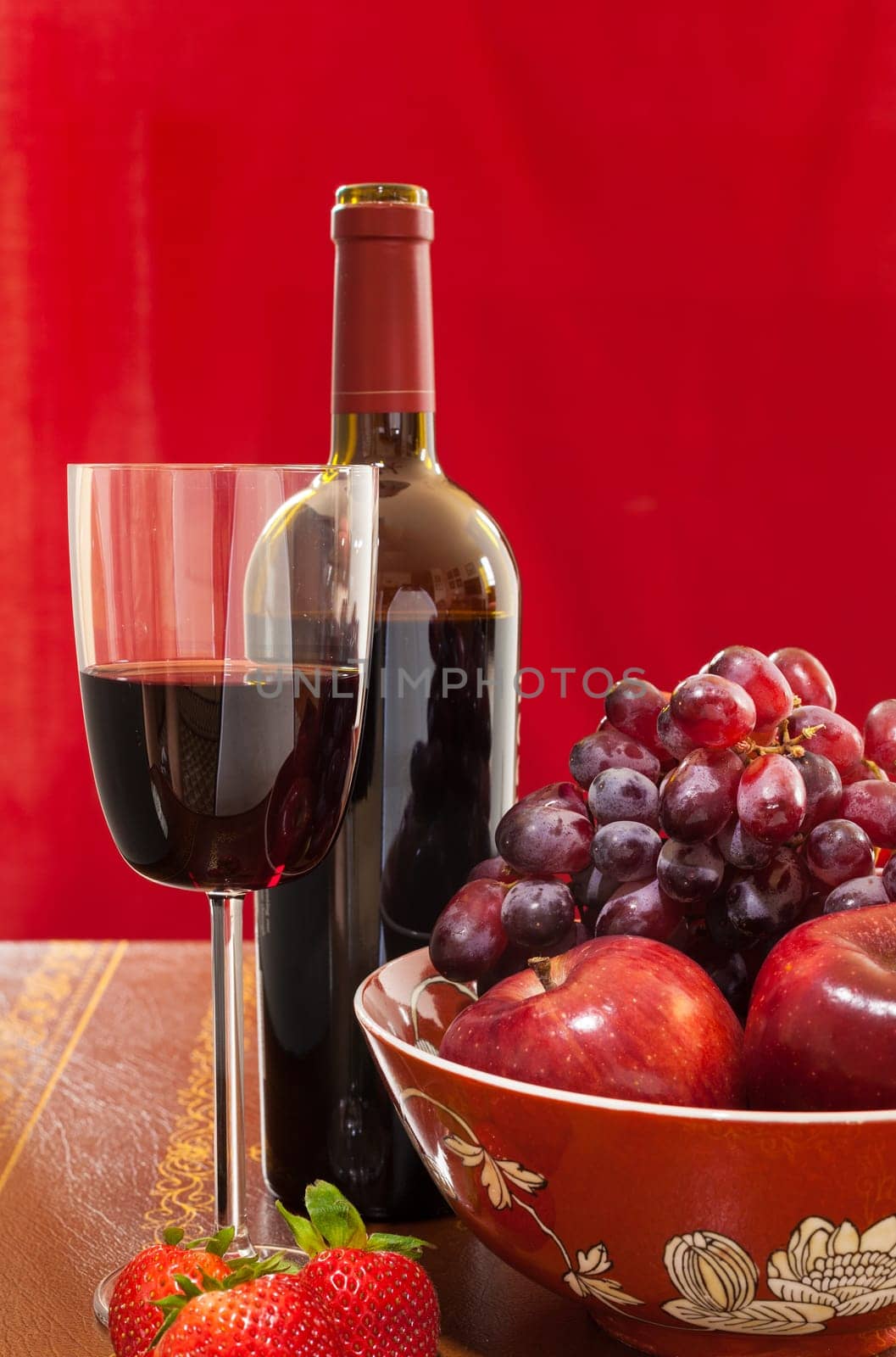 Red wine bottle and red wine in glass with red apples, grapes and strawberries