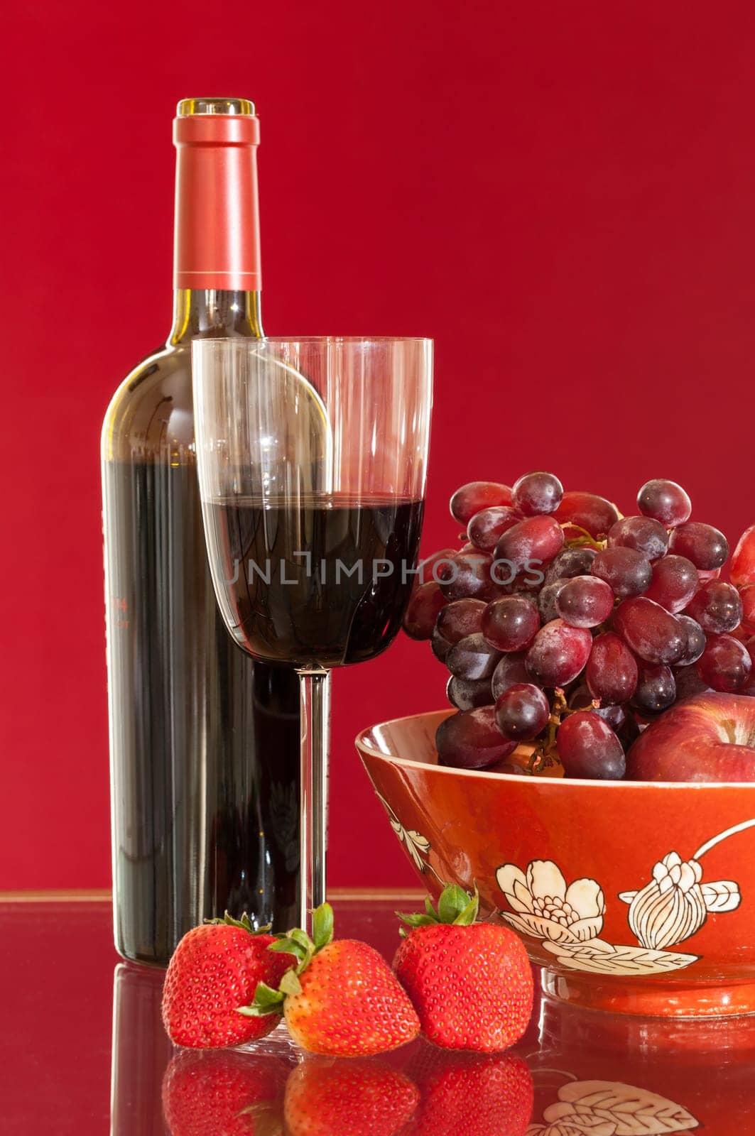 Red wine bottle and red wine in glass with red apples, grapes and strawberries