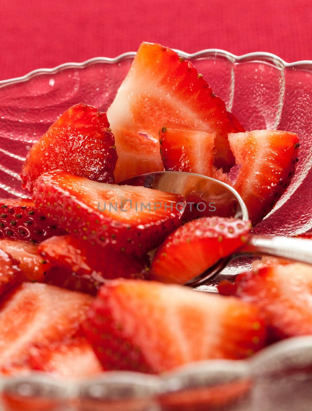 Glass dish with freshly sliced strawberry fruits against a red tablecloth