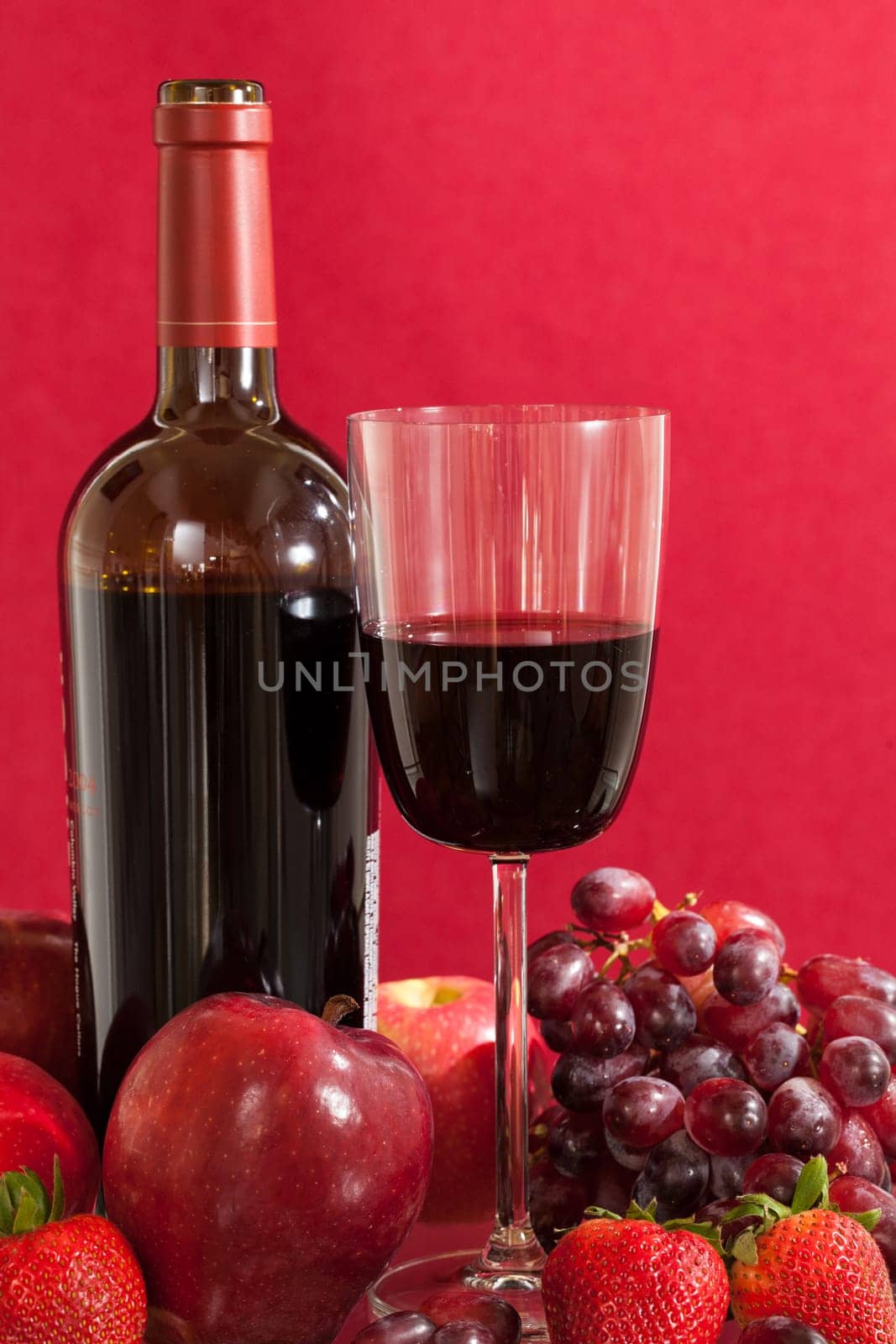 Red wine bottle and red wine in glass with red apples, grapes and strawberries