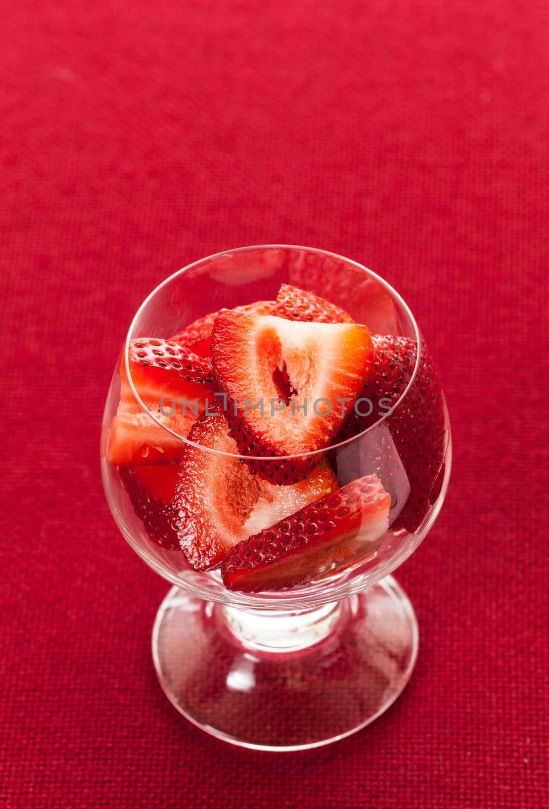 Glass dish with freshly sliced strawberry fruits against a red tablecloth