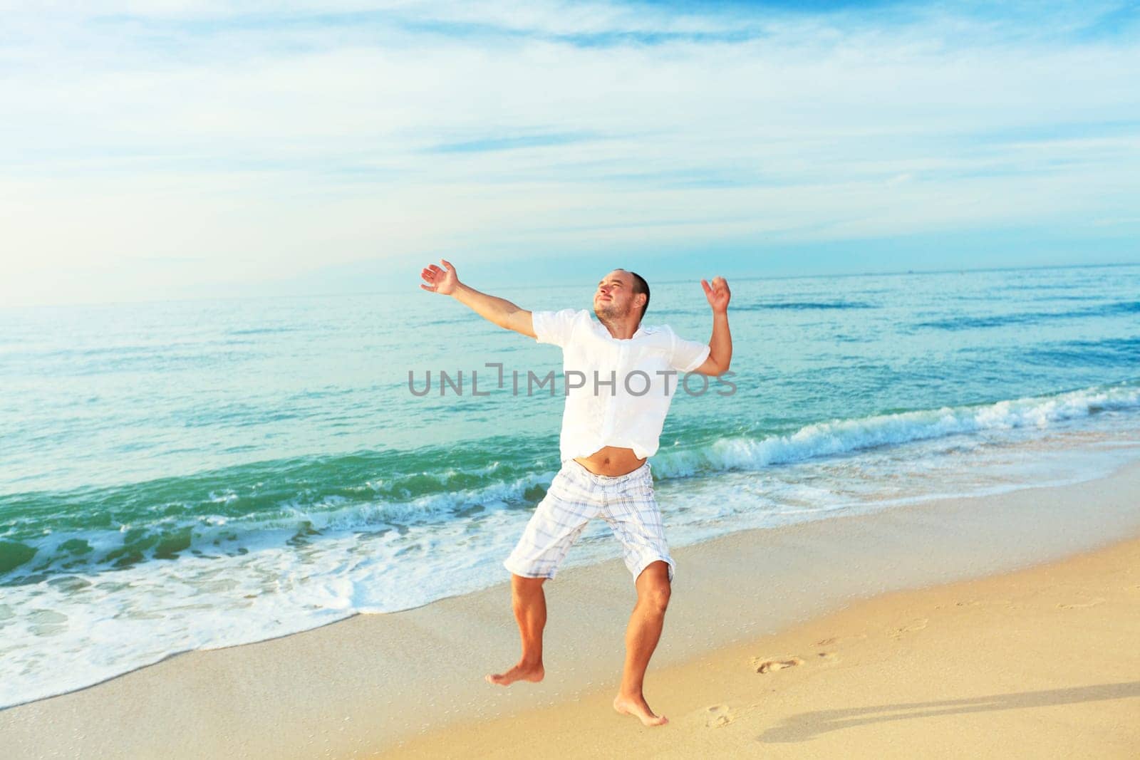 Happy man jumping on the beach at sunrise