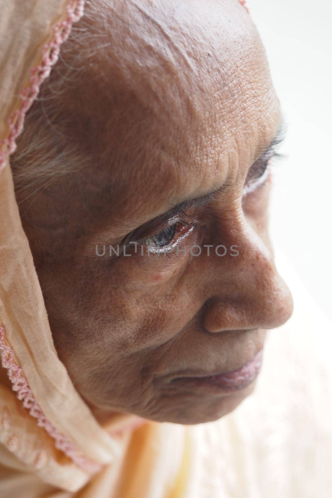 An elderly woman gazes thoughtfully while wearing a light scarf.